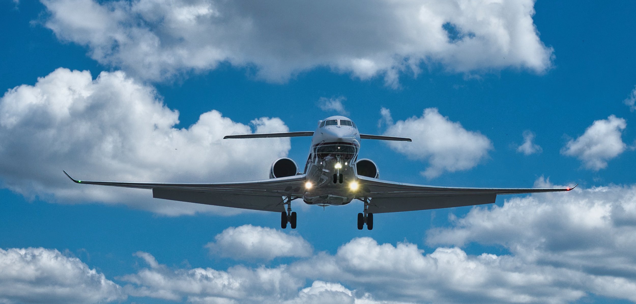An airplane flying low in a clear blue sky with scattered white clouds.