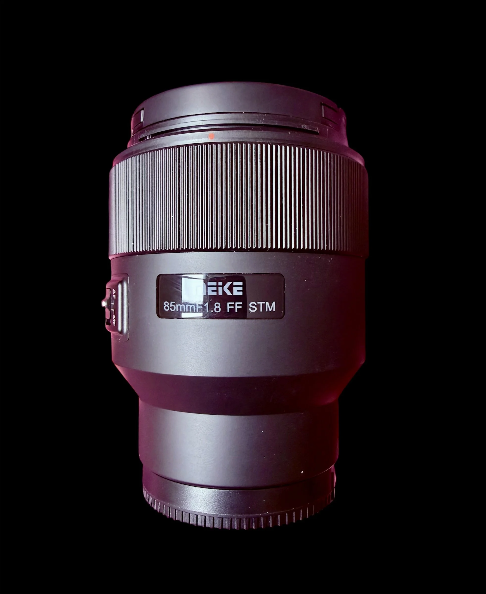 Close-up of camera lens with black background, showing details and specifications such as 85mm 1.8 FF STM.