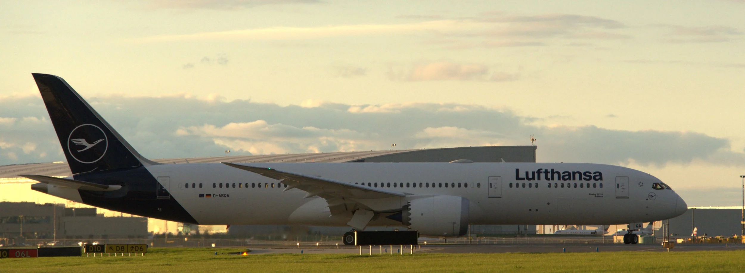 Lufthansa Boeing 777 airplane on the tarmac at sunset with a partly cloudy sky in the background.