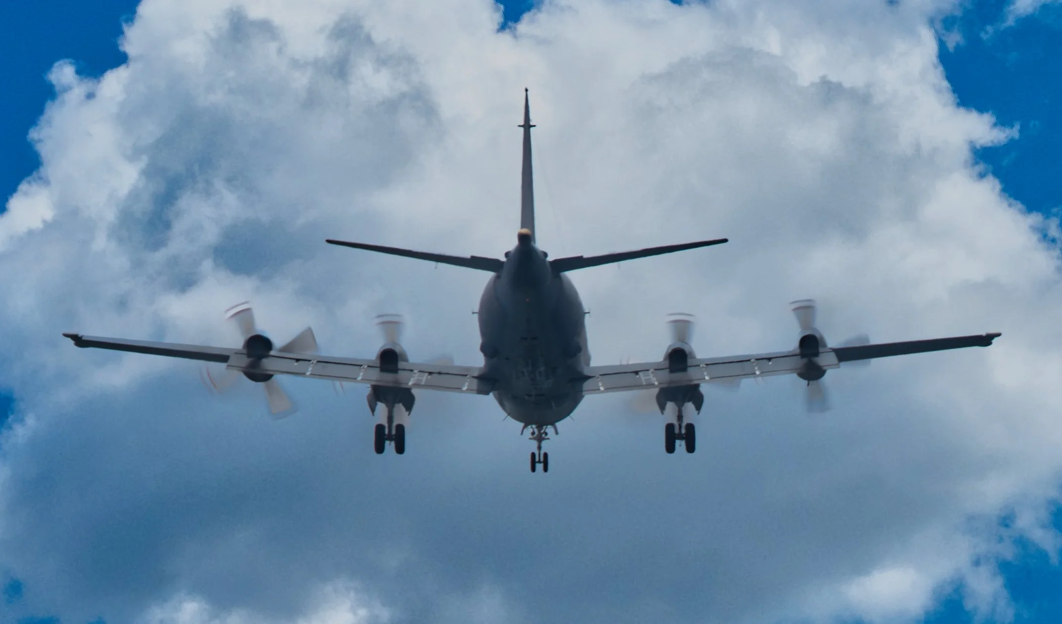 View of a military aircraft flying in the sky with clouds, seen from below