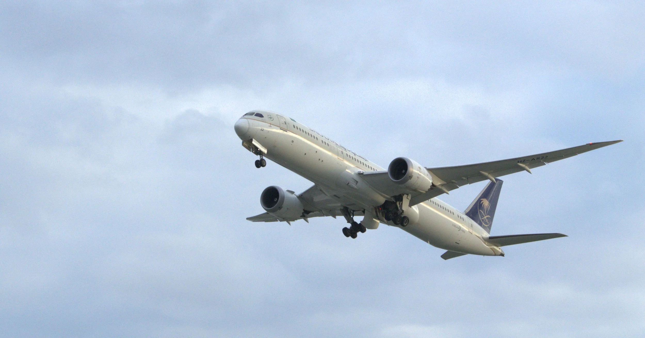 A large commercial airplane in flight against a cloudy sky, with landing gear still extended.