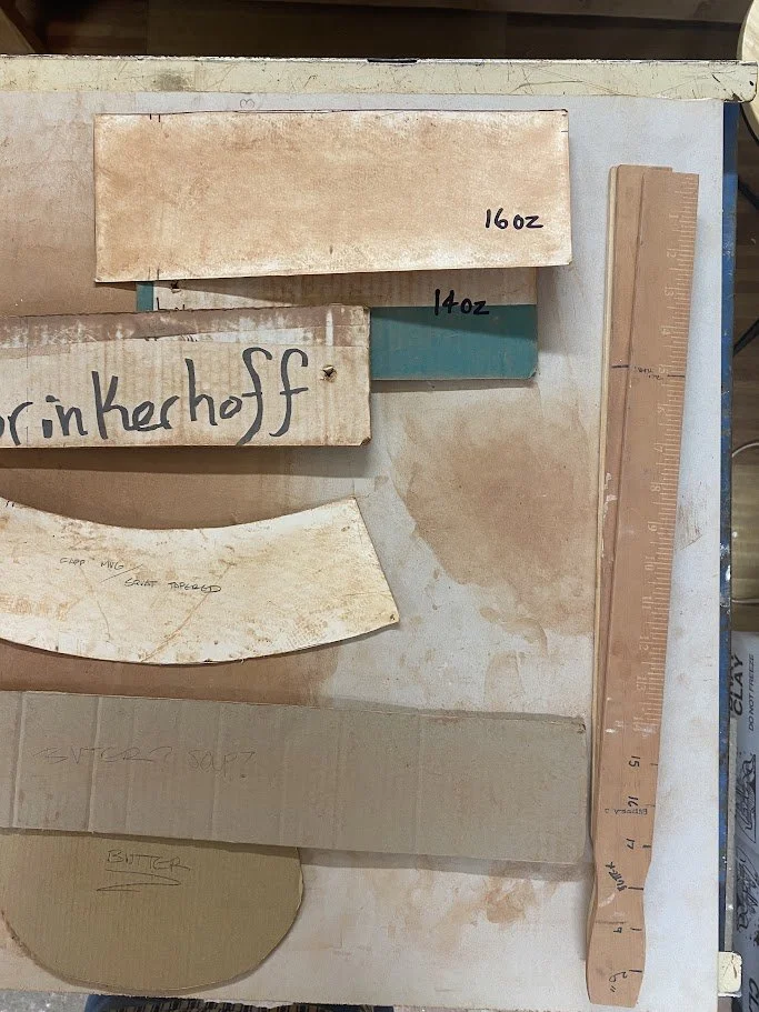 Various ceramic or clay pieces with handwritten labels indicating weights, a wooden ruler, and partially visible tools on a worktable.