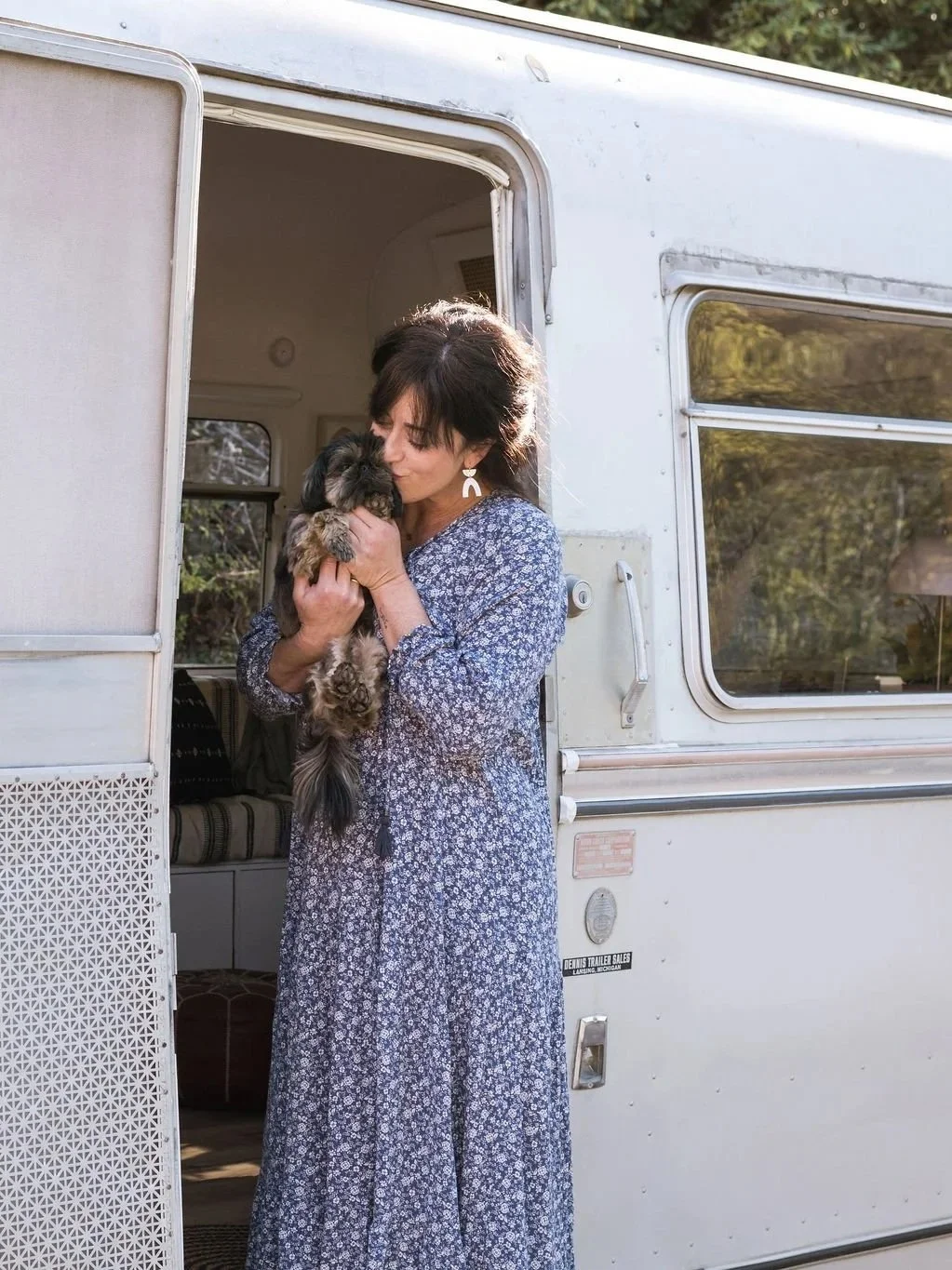A woman holding a small puppy in front of a white camper trailer.