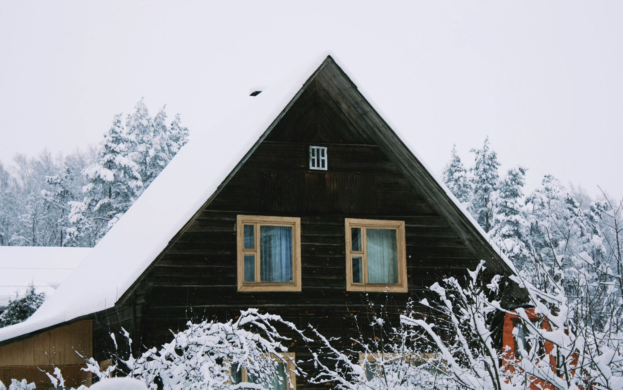 brown A-frame cabin surround by trees in the snow