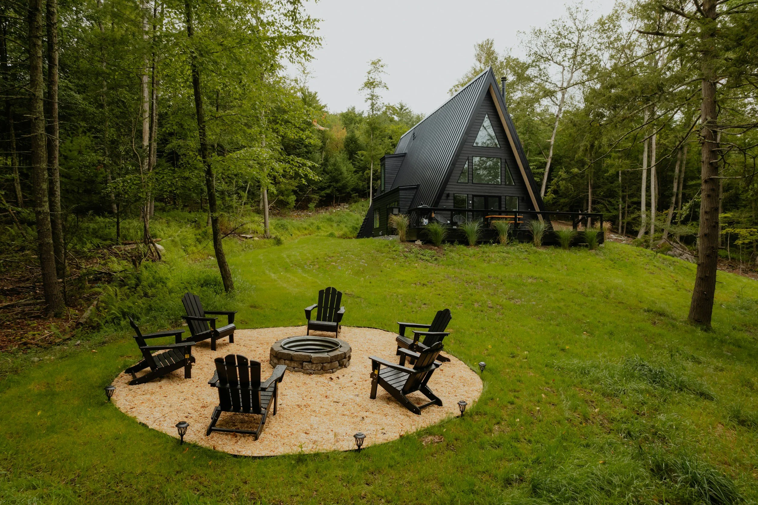 black a-frame cabin with firepit in the forest
