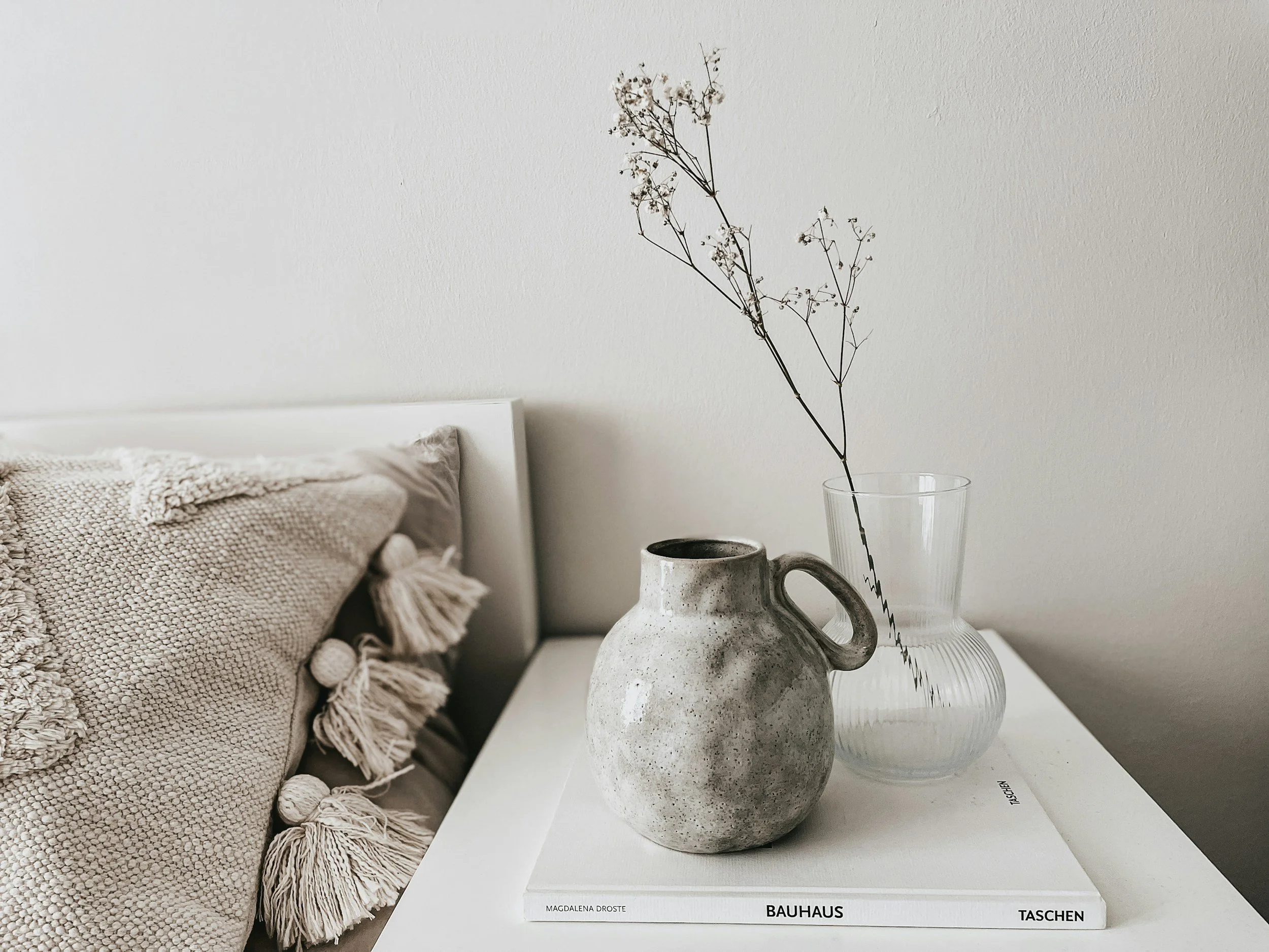 ceramic vase on white nightstand next to natural throw pillow