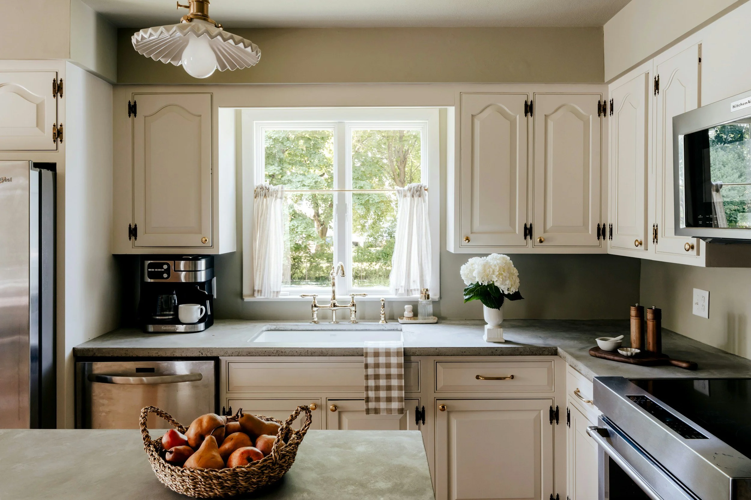 kitchen with white cabinets a basket of pears and a window above the sink