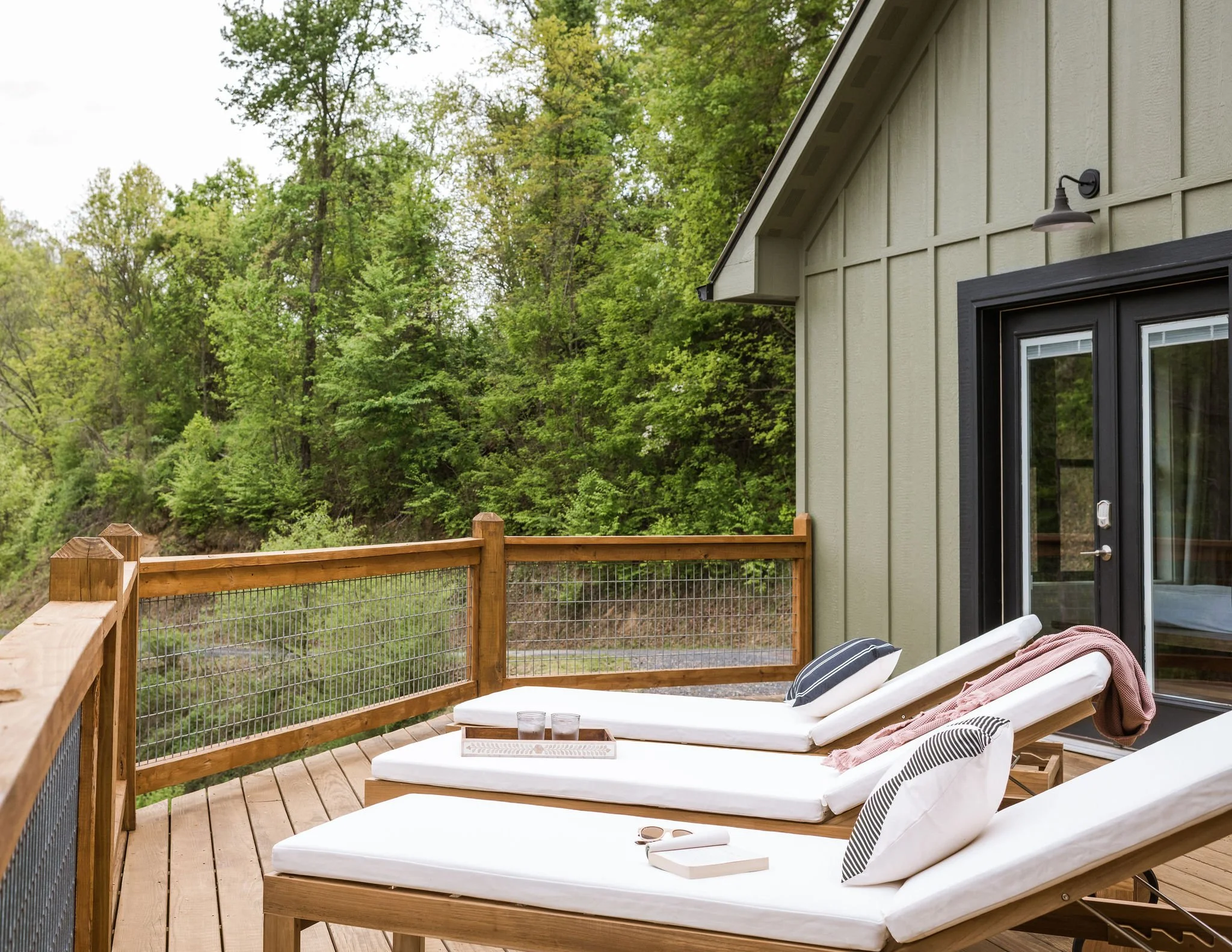white lounge chairs on a wood deck in front of a green house