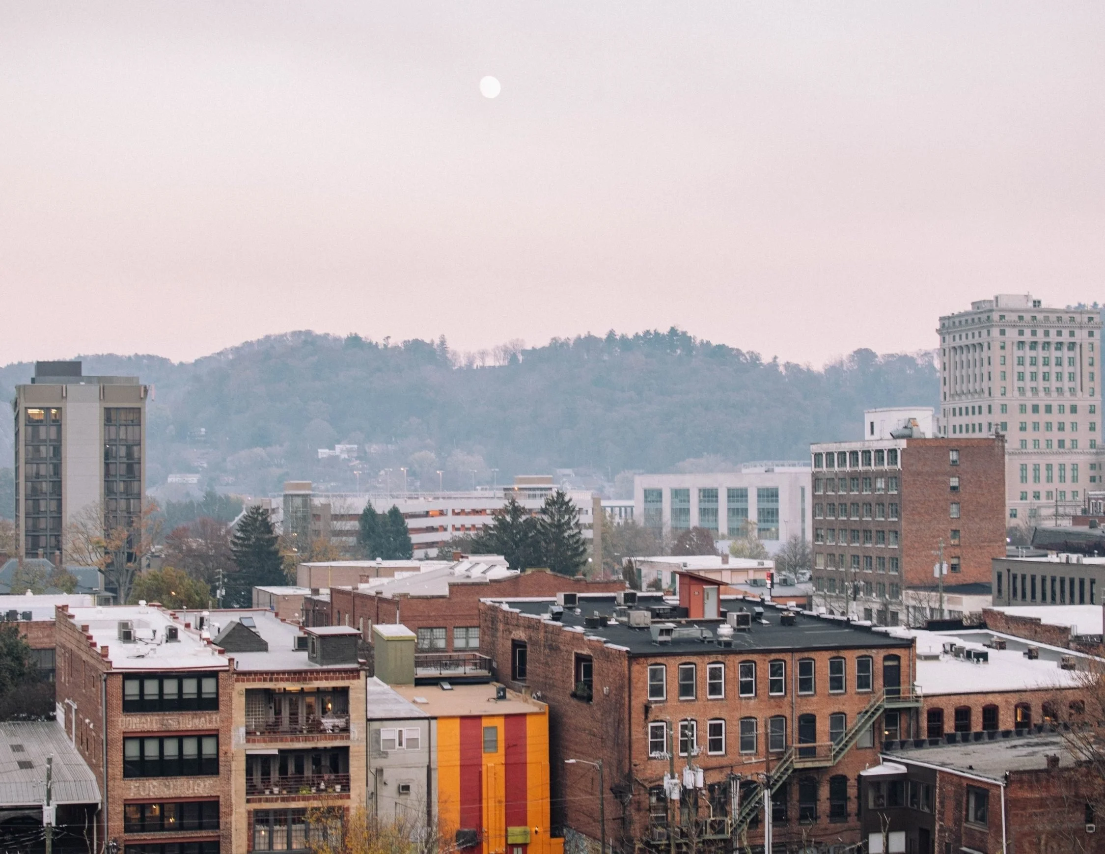 asheville skyline with mountains and a full moon with a pink sky