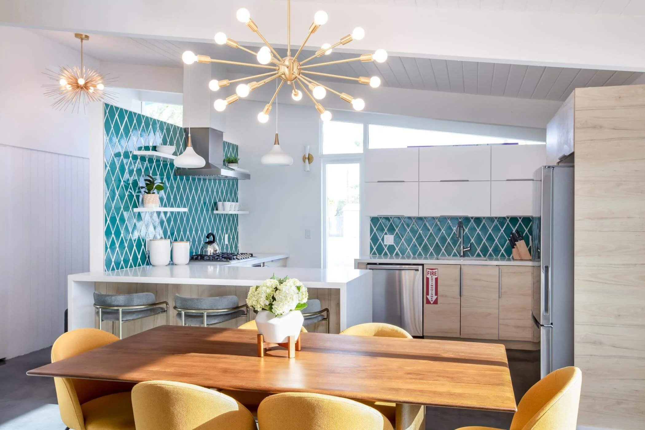 yellow dining chairs with sunburst pendant light and teal tile backsplash