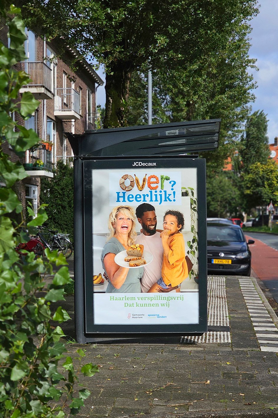 A poster on a sidewalk advertising Haarlem, featuring a smiling woman, a man, and a child, with the woman holding a plate of food. Spaarnelanden 