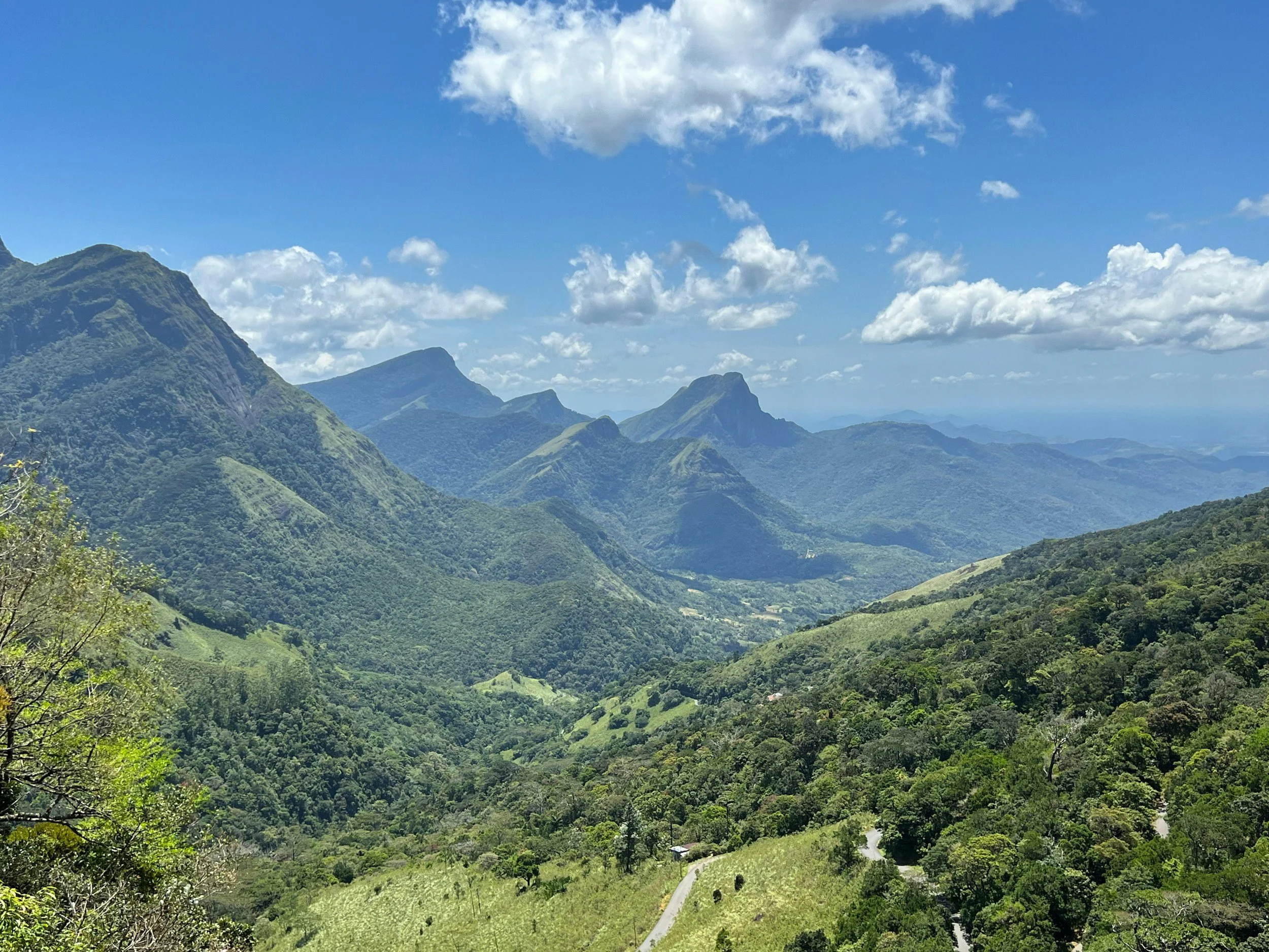 Scenic view of green rolling hills and mountains under a blue sky with scattered clouds.