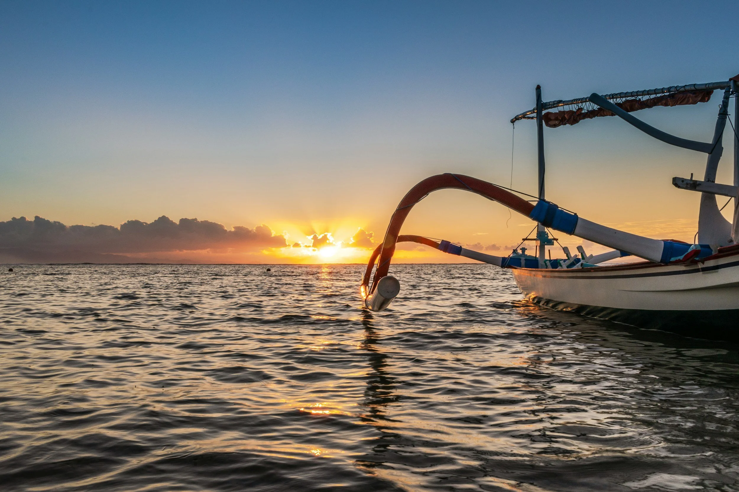 A boat with a water slide attached on the water during sunset.