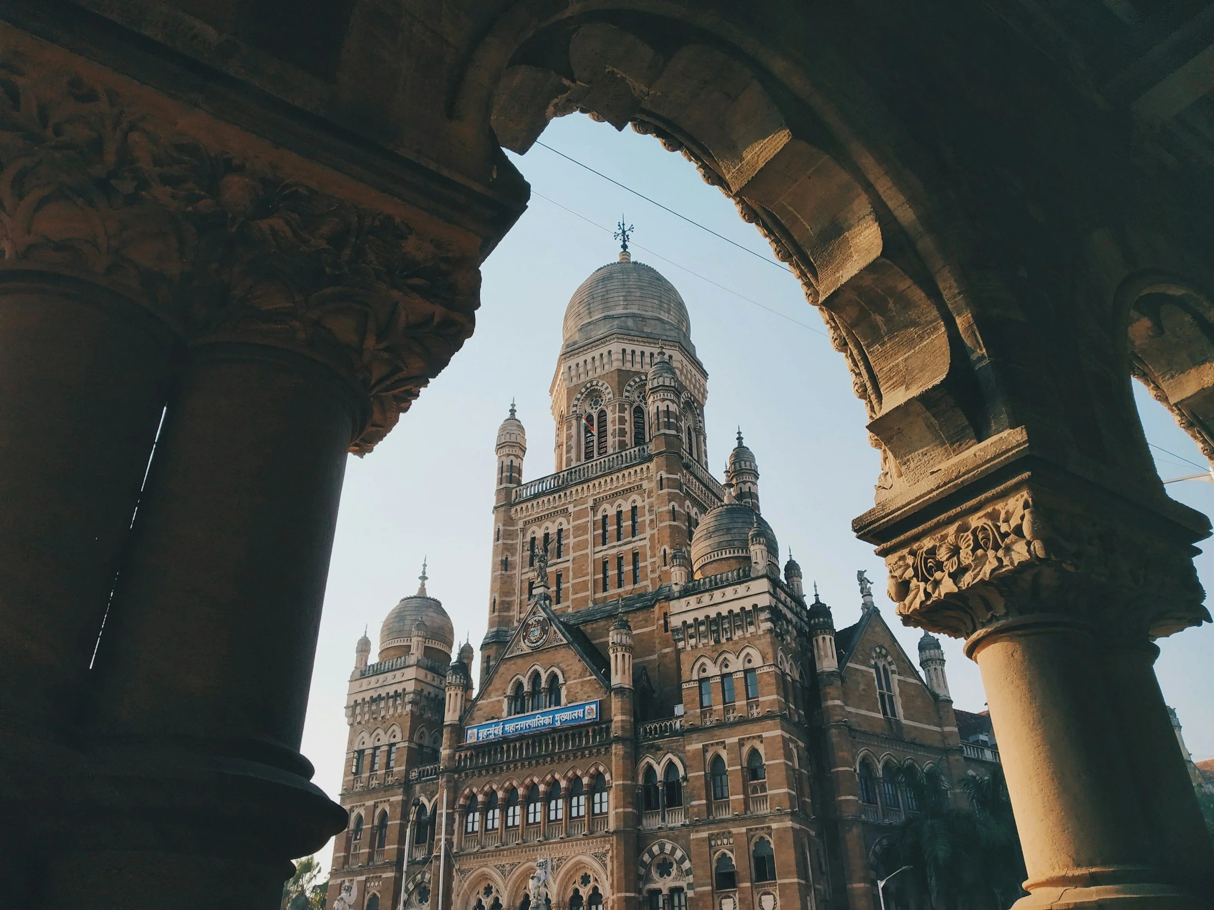 View of a historic building with multiple towers and domes, seen through ancient stone carved pillars with detailed patterns, under a clear sky.