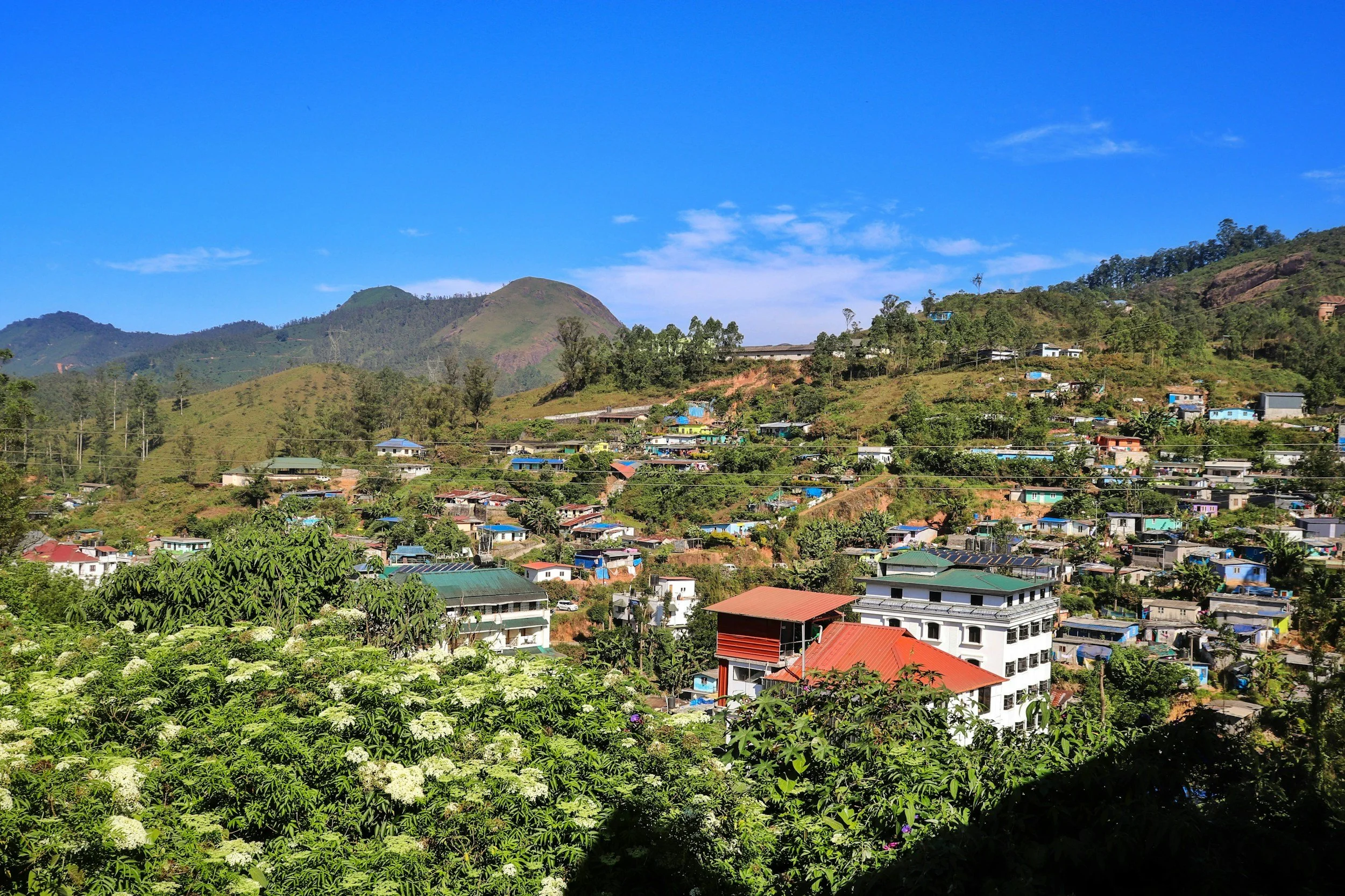 Hilly landscape with houses and greenery under a blue sky with scattered clouds