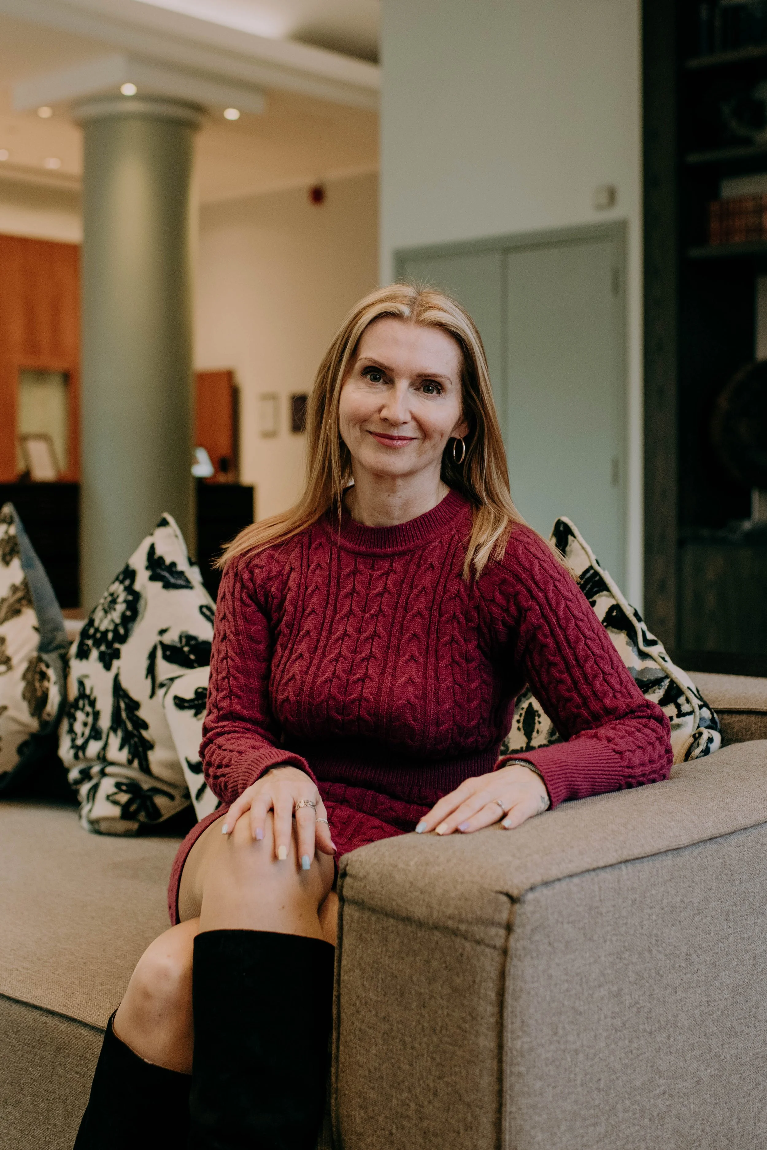 Portrait of a woman with red hair in a burgundy sweater sitting on a sofa cushions in a living room
