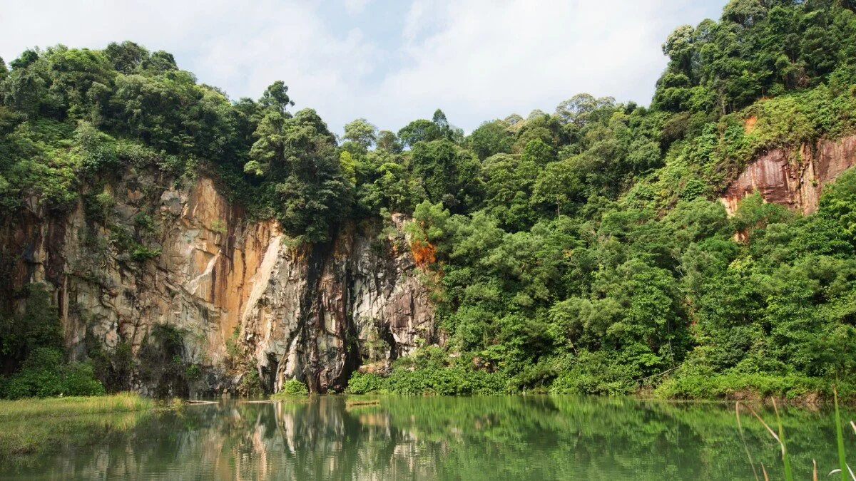 A lush green forest with rocky cliffs surrounds a calm reflective body of water.