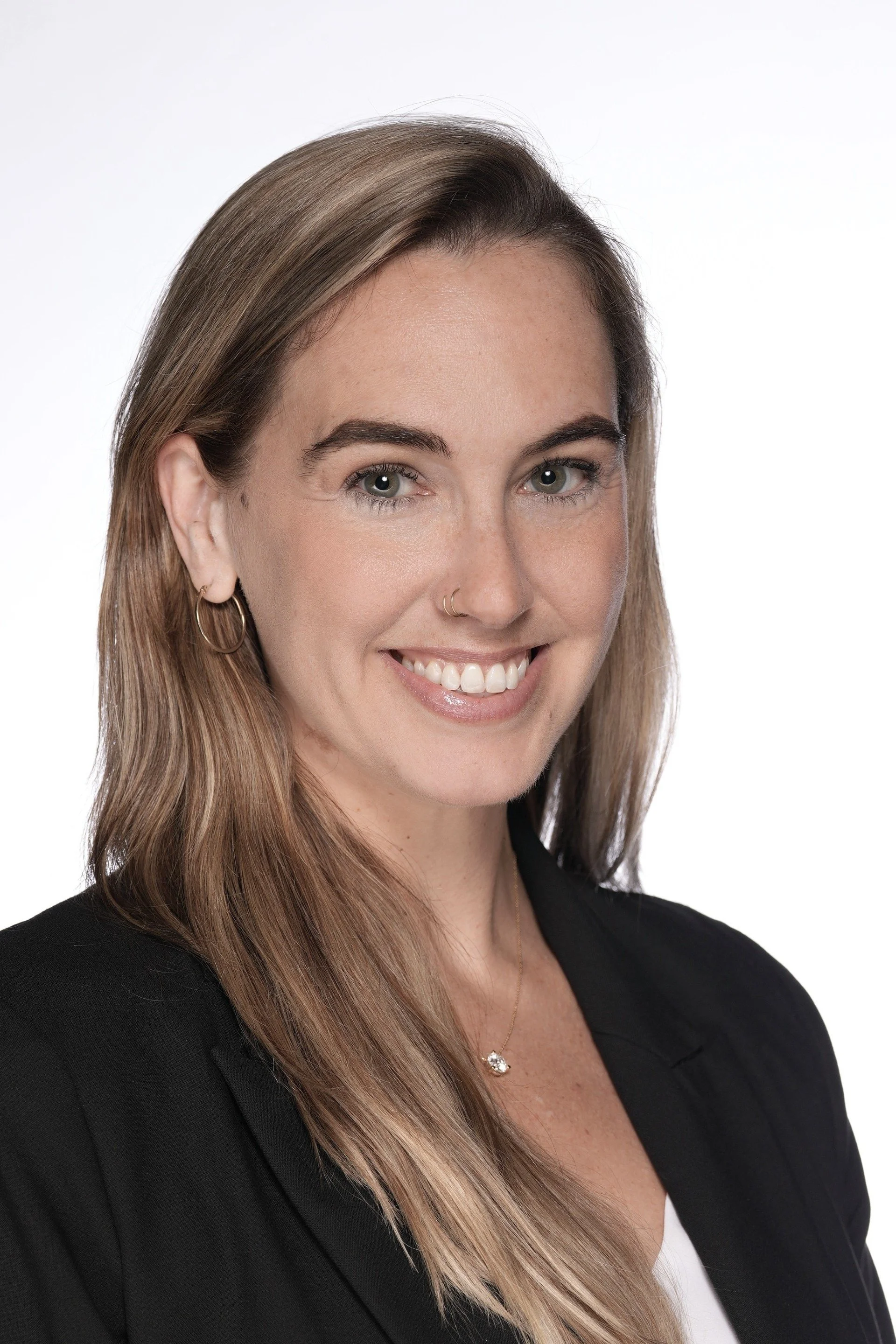 A woman with long brown hair, blue eyes, and light skin, smiling, wearing a navy blue top, against a white background.