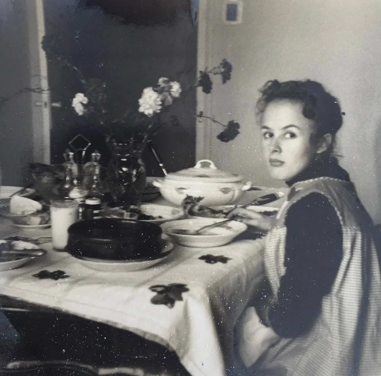 1960s black and white photograph of a young woman at a family dinner table in Bilbao.