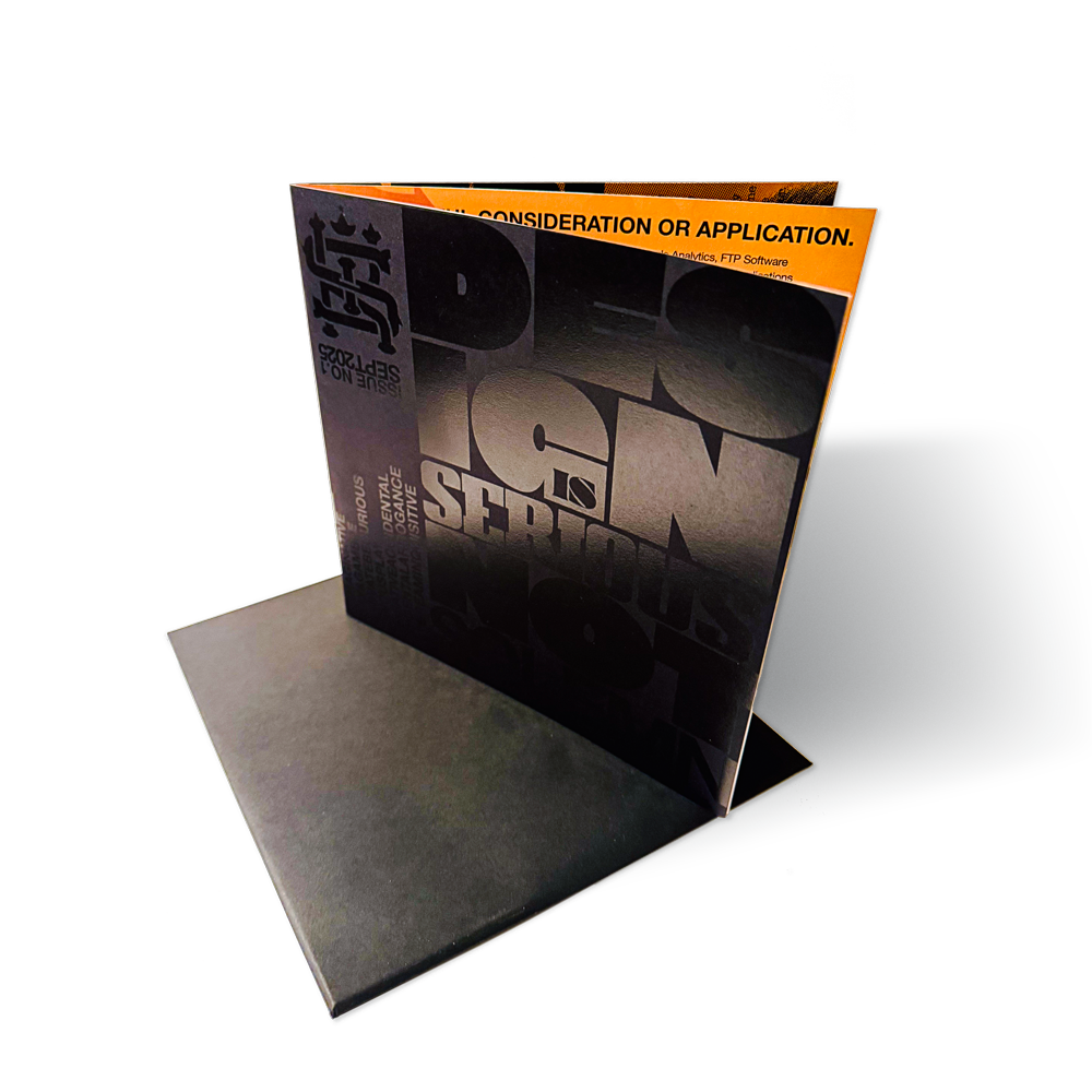 A brochure standing in a presentation folder on a desk, with a black cover and orange insert visible at the top edge.