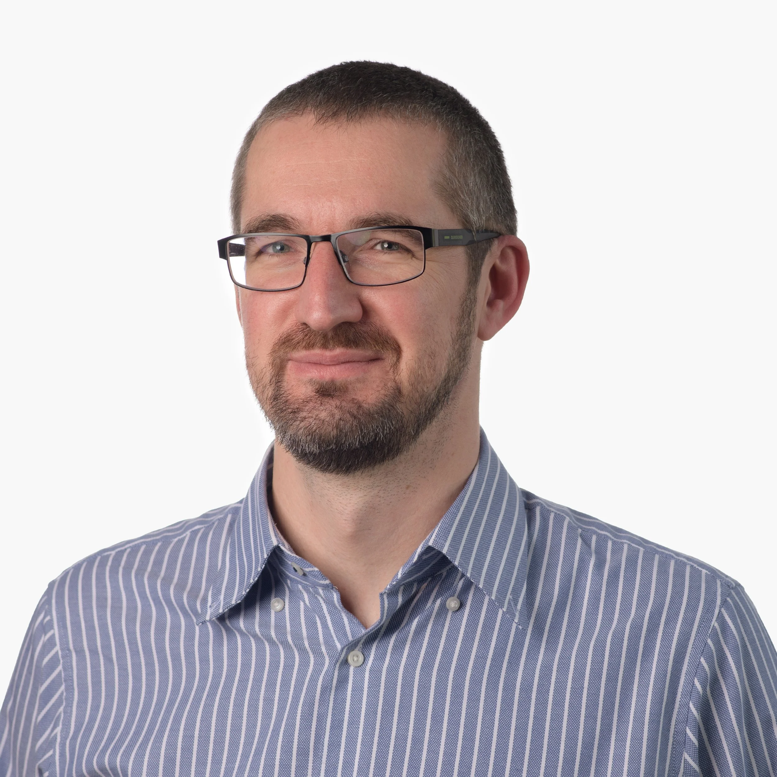 A man with short hair, glasses, and a beard wearing a blue and white striped dress shirt, posing against a white background.