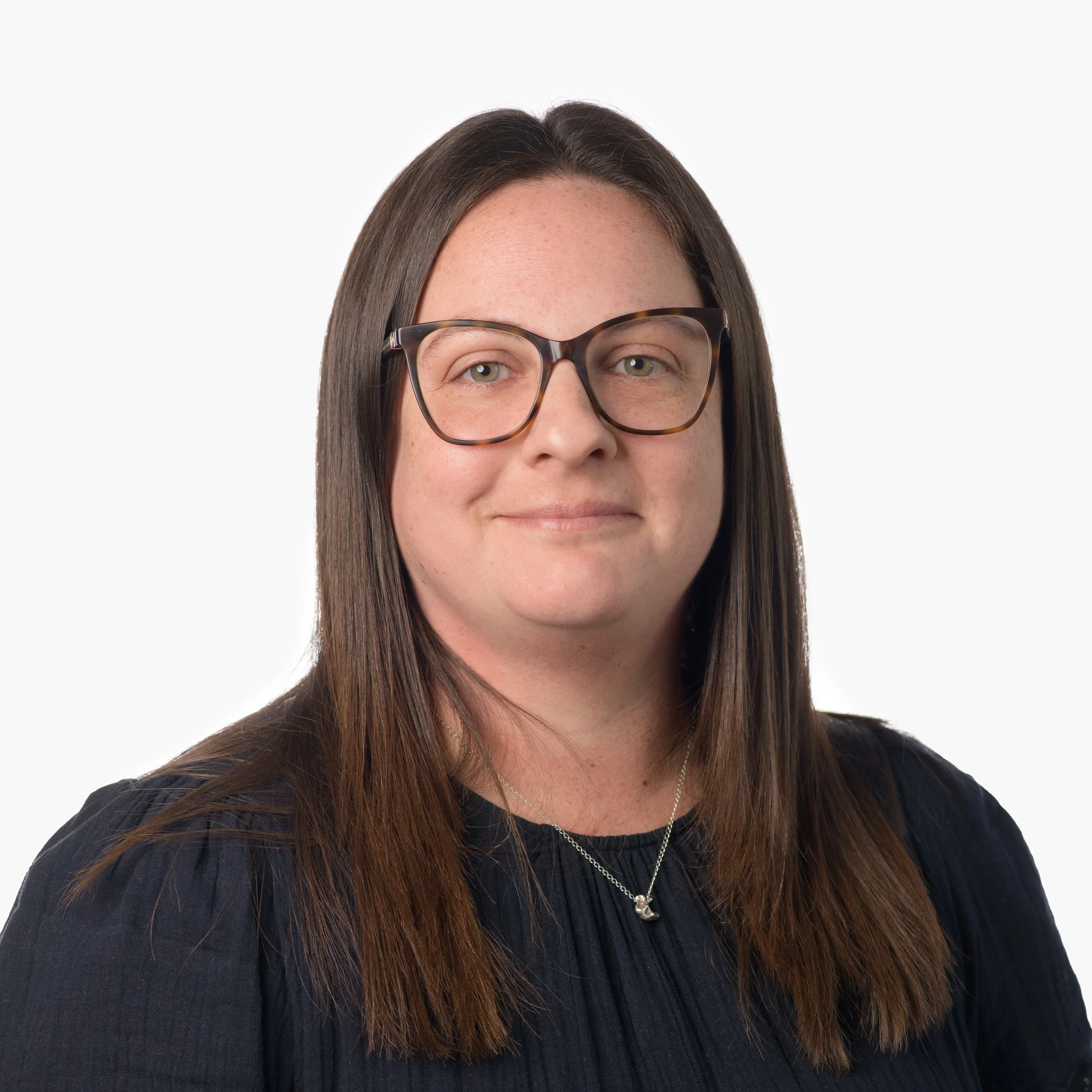 Portrait of a woman with long brown hair, glasses, and a black top, smiling slightly against a plain white background.