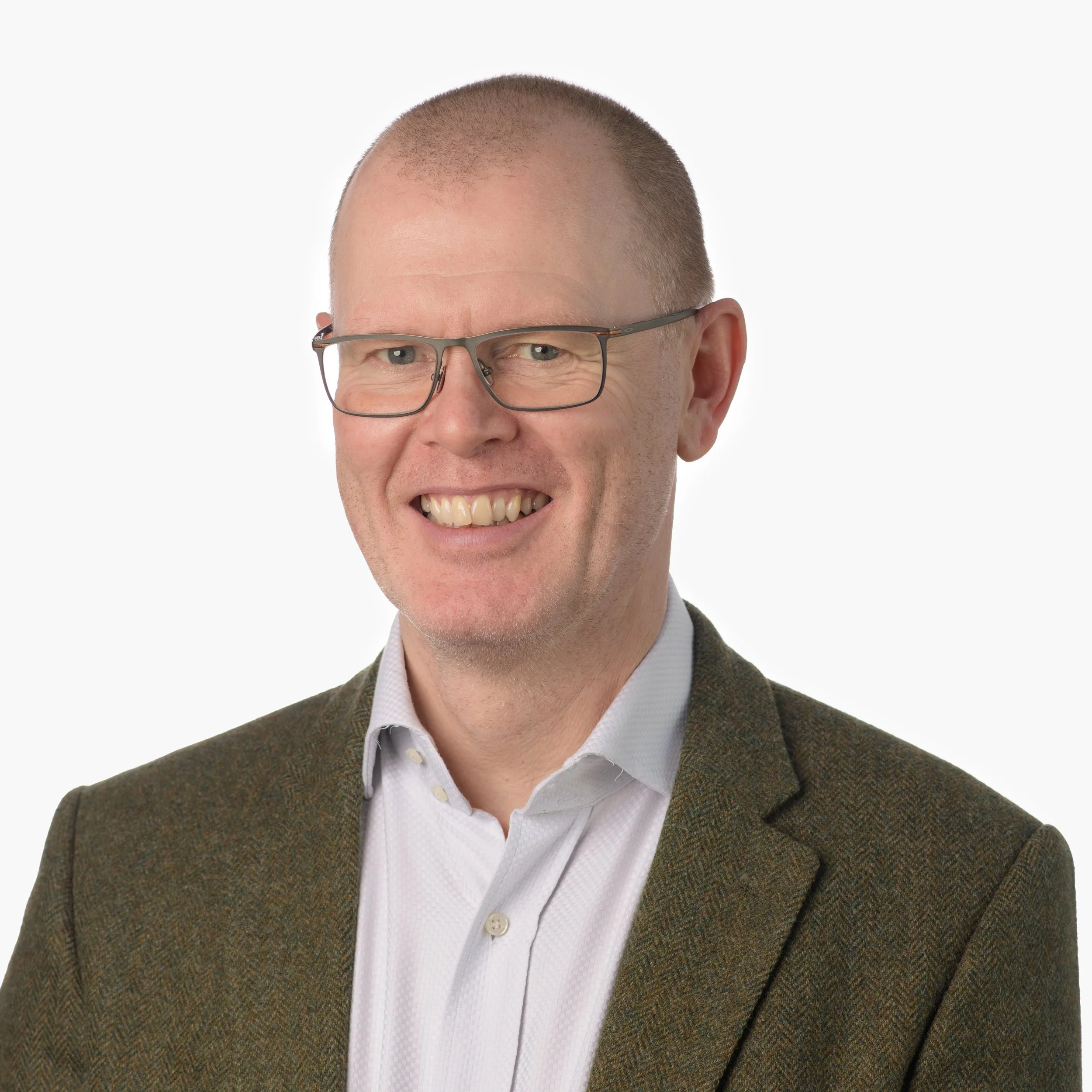 A smiling man with glasses, wearing a white shirt and brown blazer, posing against a white background.