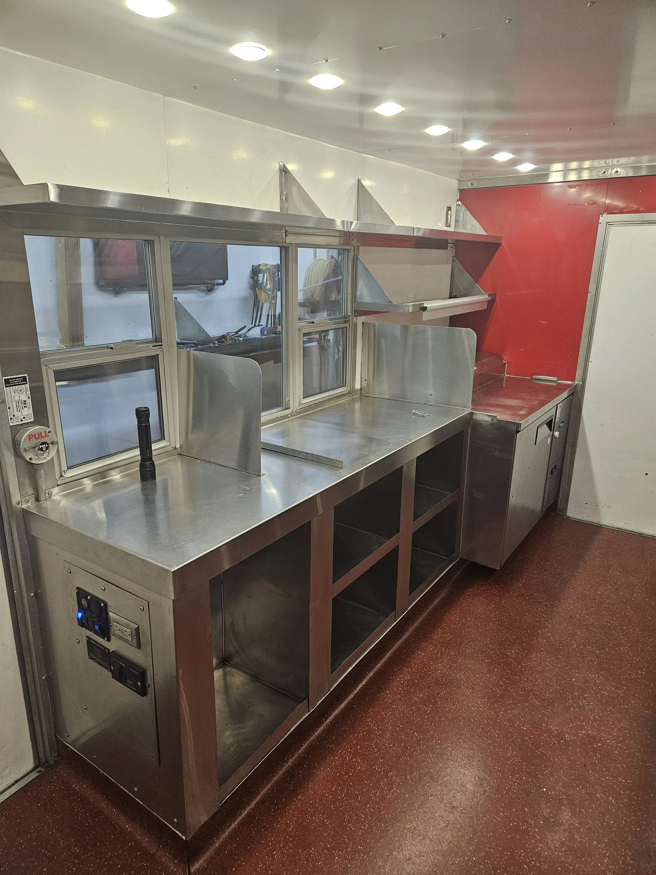 Empty stainless steel kitchen counter with a backsplash, small window, and red wall in a commercial kitchen setting.