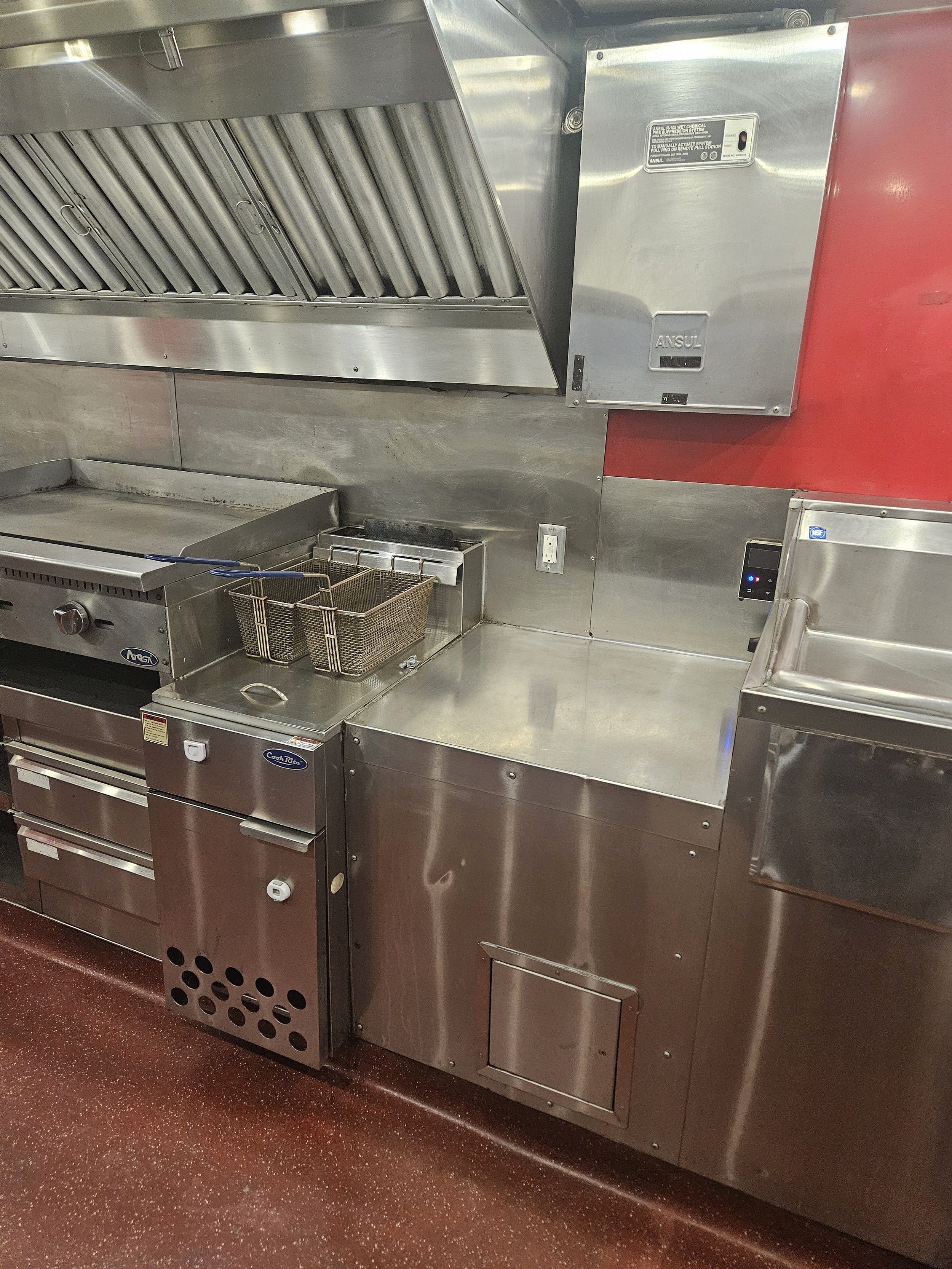 A commercial kitchen with stainless steel appliances, including a stove, fryer baskets, and an exhaust hood.