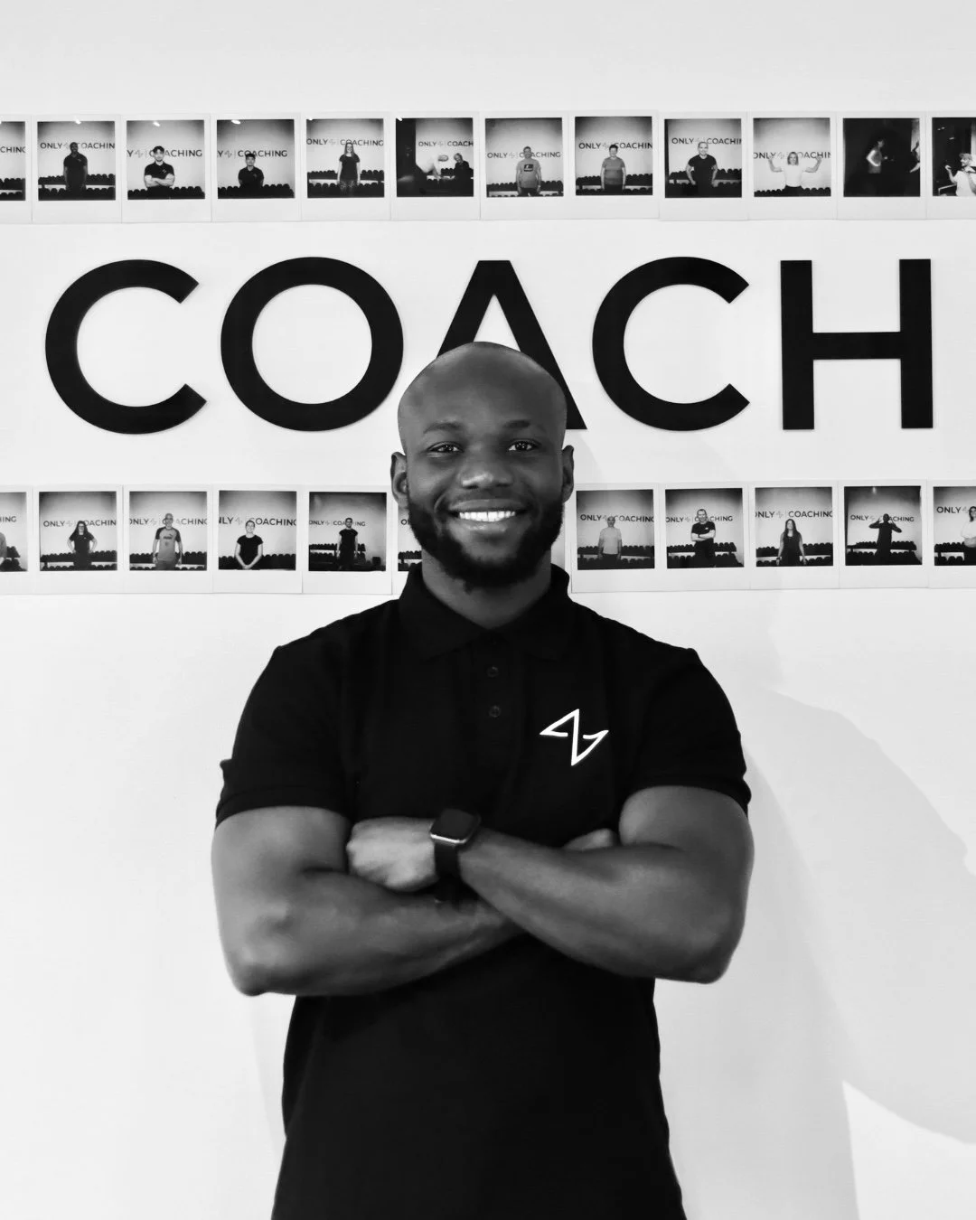 A smiling man standing with arms crossed in front of a wall with a large 'COACH' sign and a series of small photos of people in a coaching or training environment.