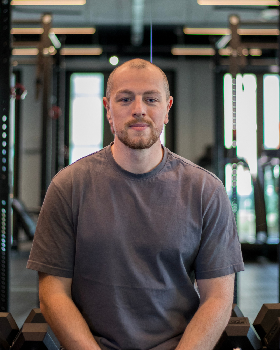 A man with a beard and short hair wearing a gray T-shirt sitting in a gym.
