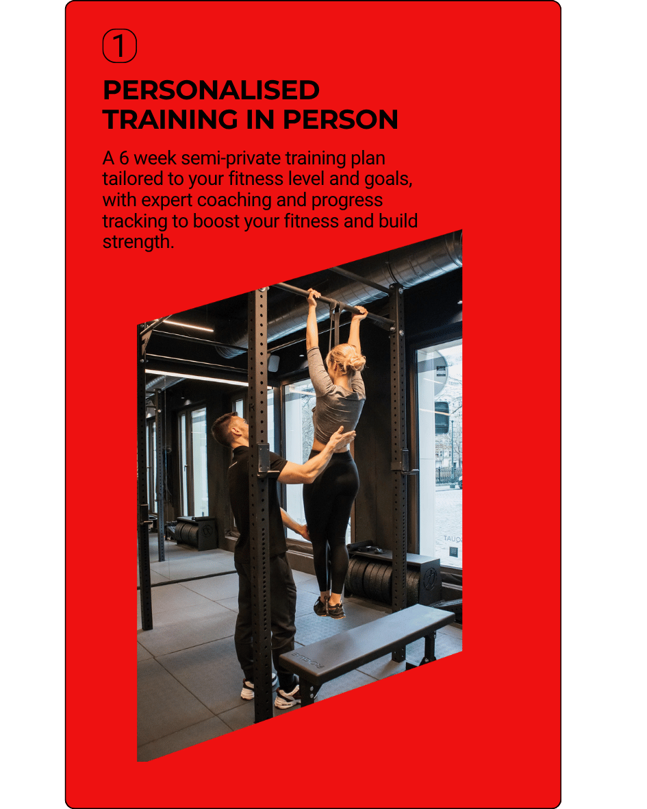 A woman working with a trainer during a personal training session at a gym. The woman is hanging from a pull-up bar while the trainer supports her.
