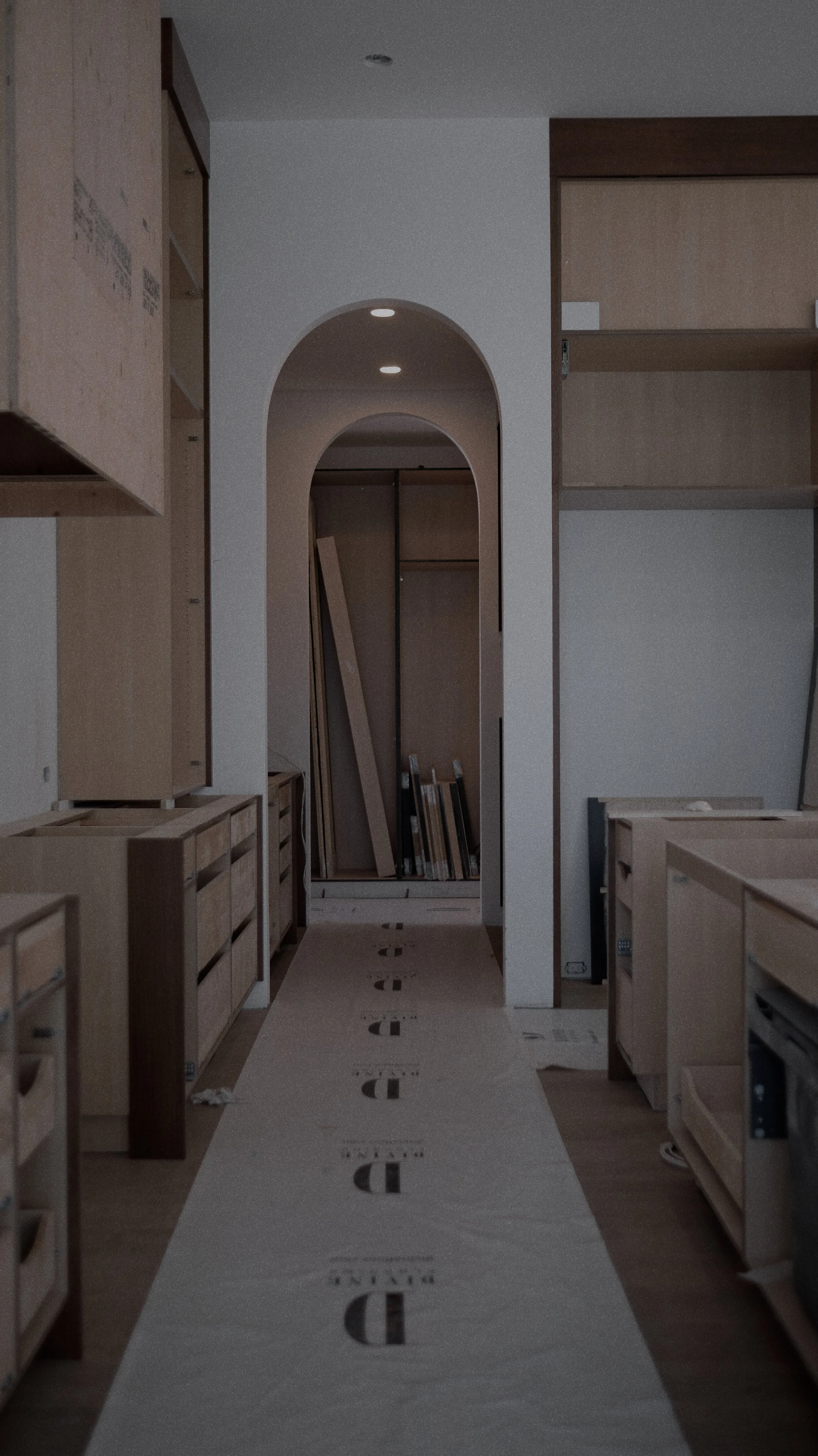 Interior of a house under construction with wooden cabinets, an arched doorway, and flooring protection.