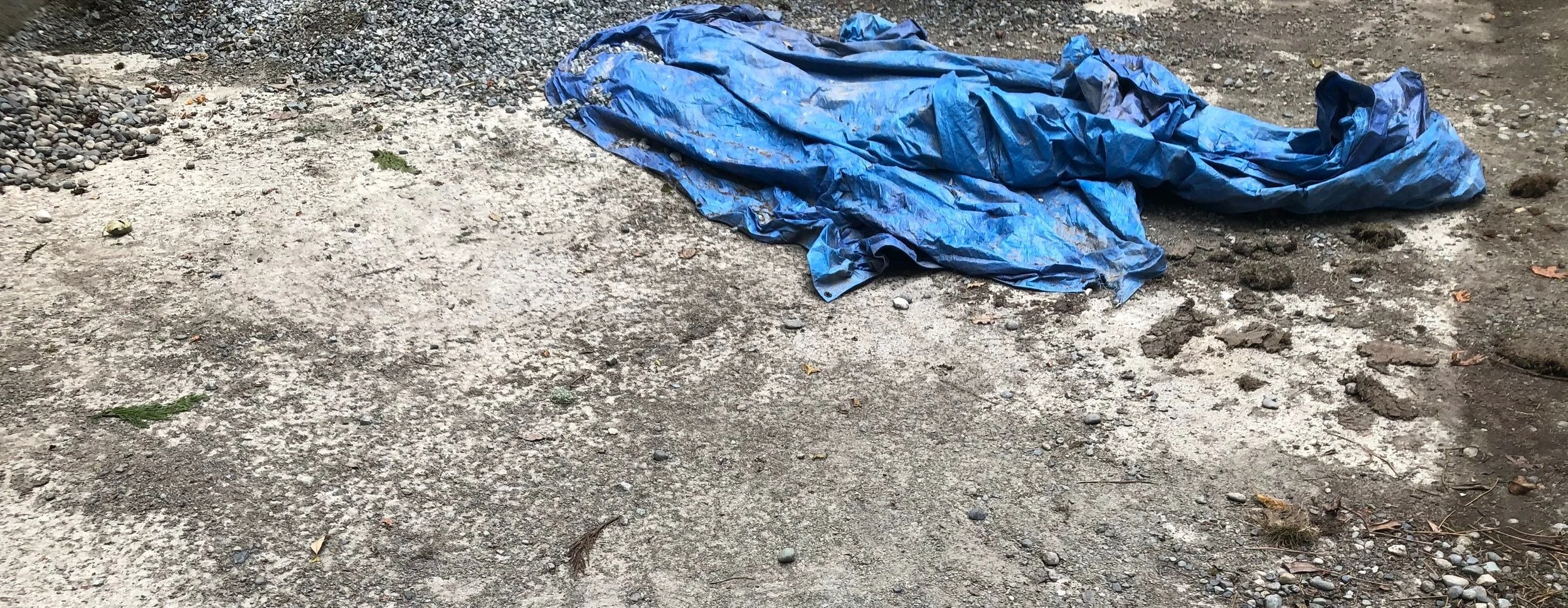 a blue tarp sculpturally lying in a pile on a concrete and gravel surface