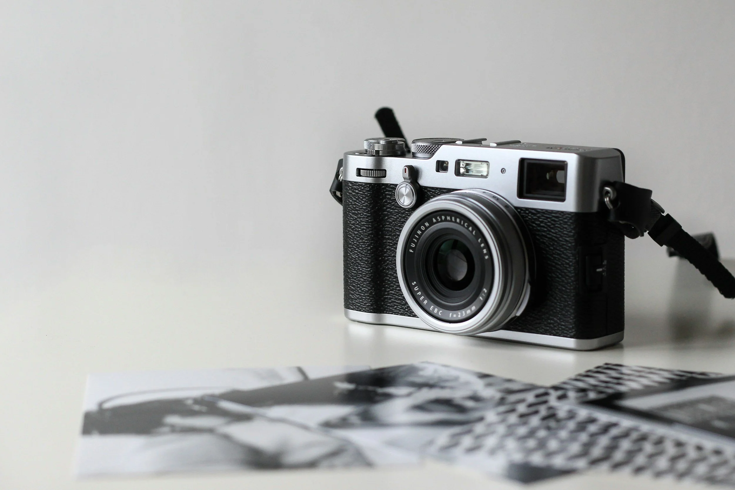 A vintage-style camera with a zoom lens placed on a white surface, with black and white photographs scattered in the foreground.