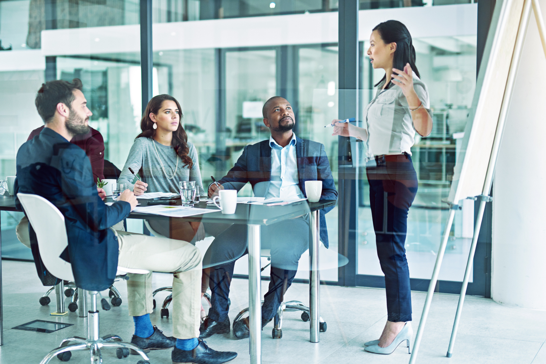 Businesswoman giving a presentation to four professionals in an office conference room.