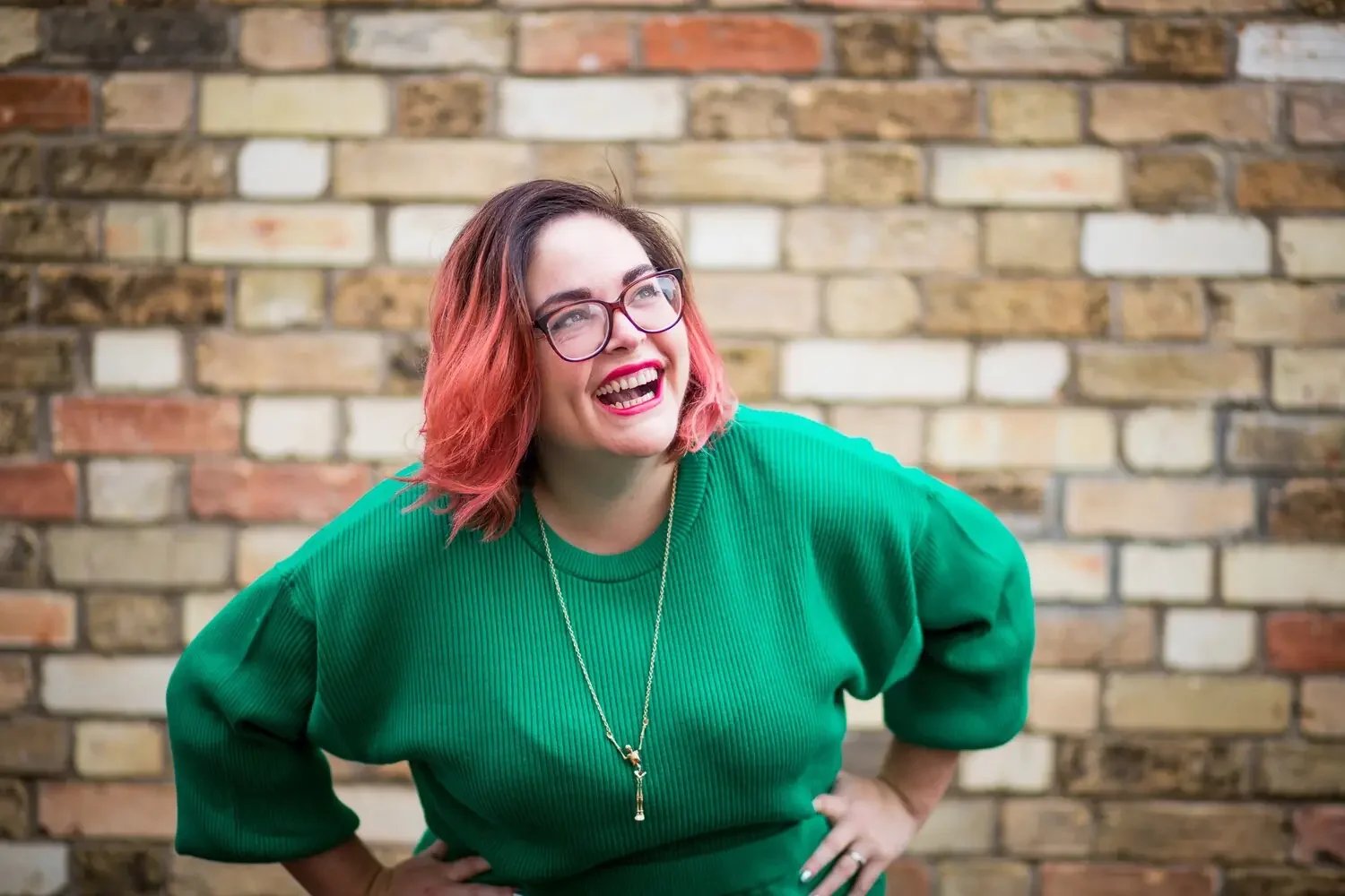 Smiling woman in green jumper against brick wall background