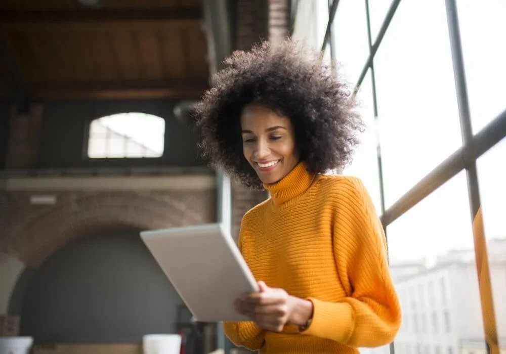 Person in orange sweater using a tablet near large windows in a modern loft.