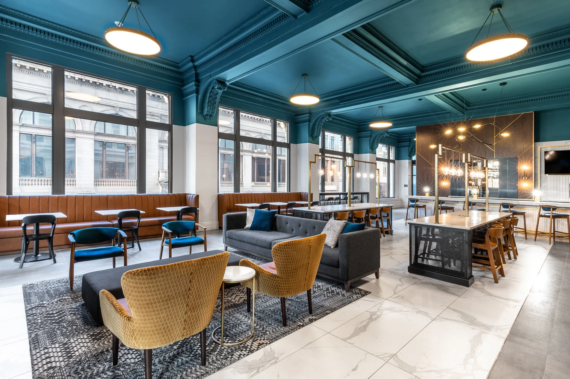 Modern lounge or cafe with teal ceiling, large windows, leather and fabric seating, and marble flooring.