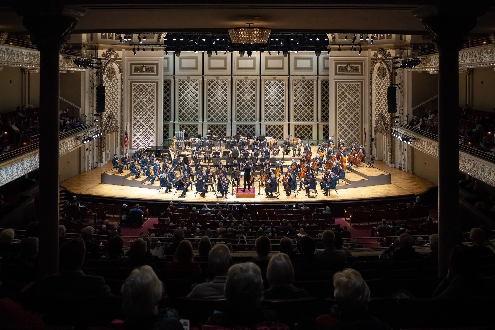 An orchestra performing on stage in a concert hall filled with audience.