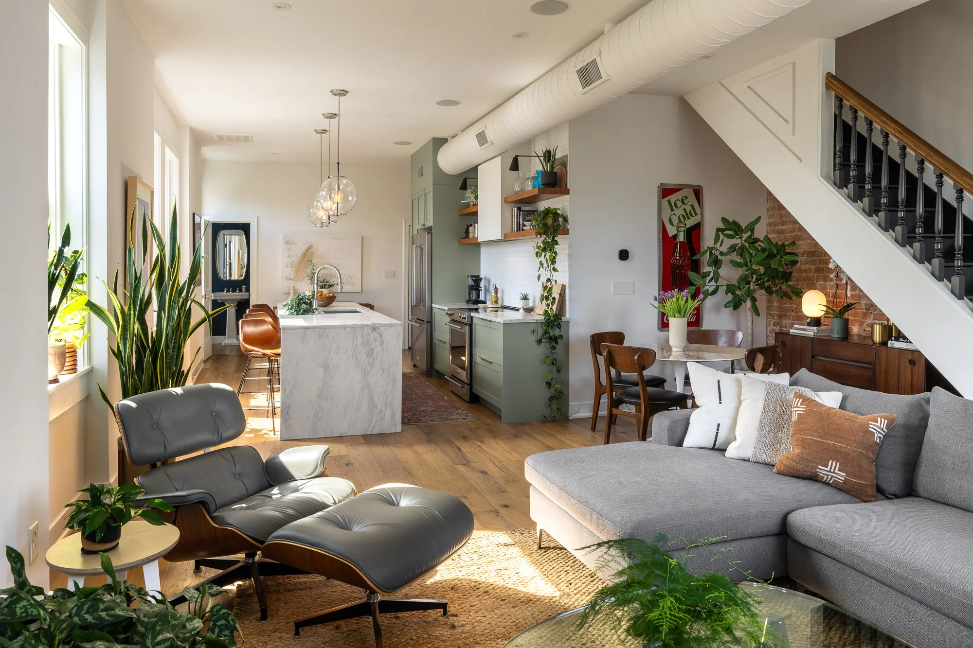 Open living room and kitchen with modern furniture, large windows, and indoor plants