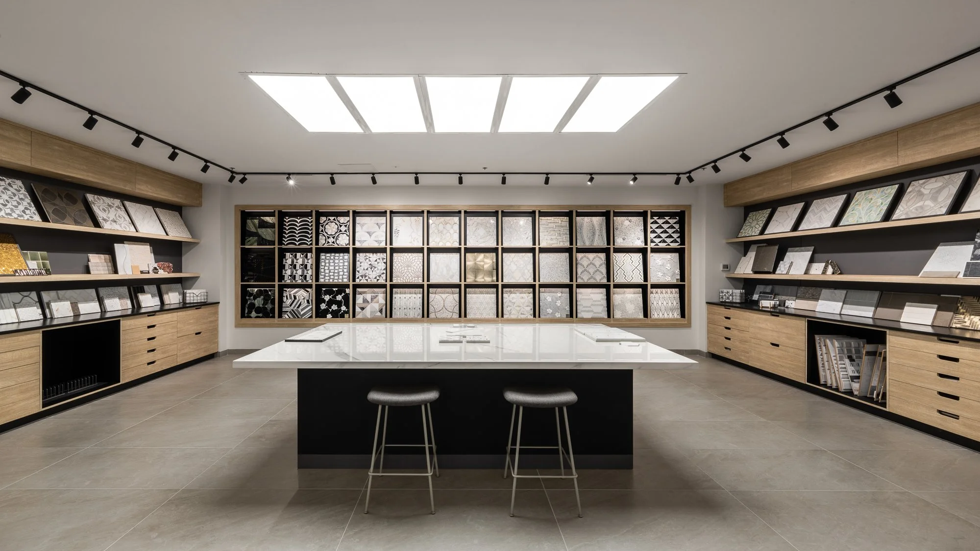 Interior of a tile showroom with display shelves full of tile samples and a central table with chairs.