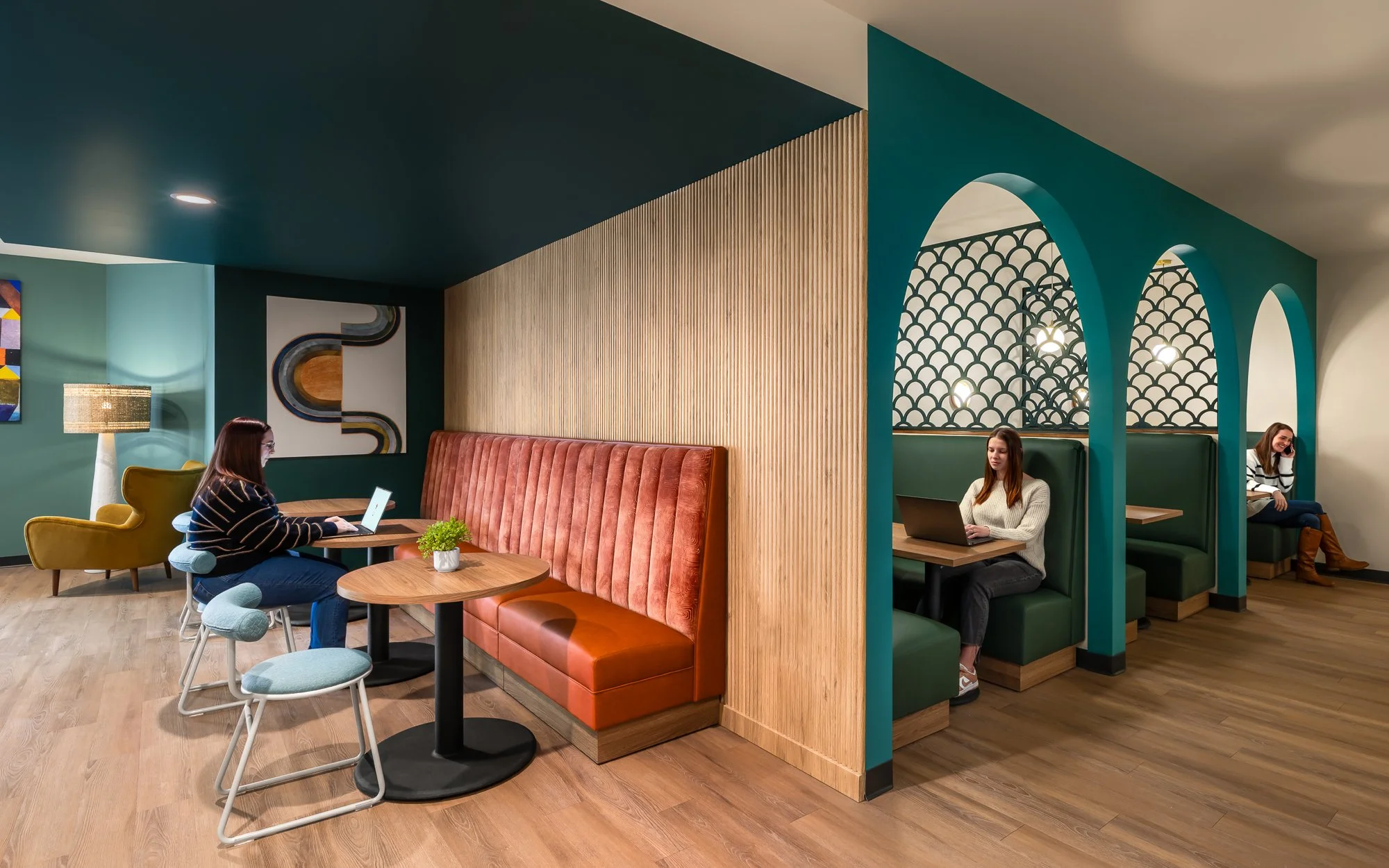 Interior of a modern cafe with colorful seating booths, artwork on the walls, and three women working on laptops at different tables.