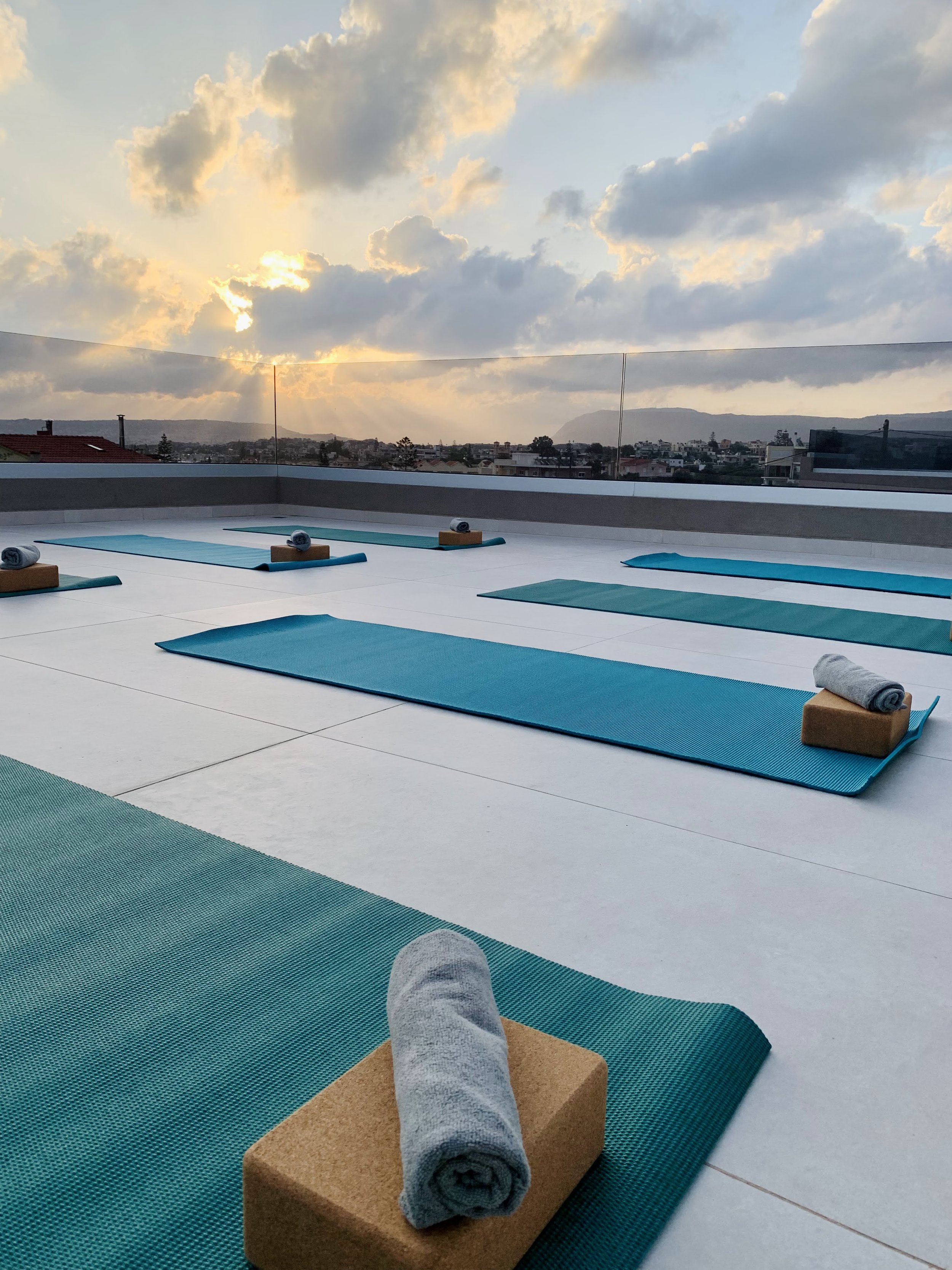 Outdoor yoga mats with blocks and towels on a rooftop at sunrise.