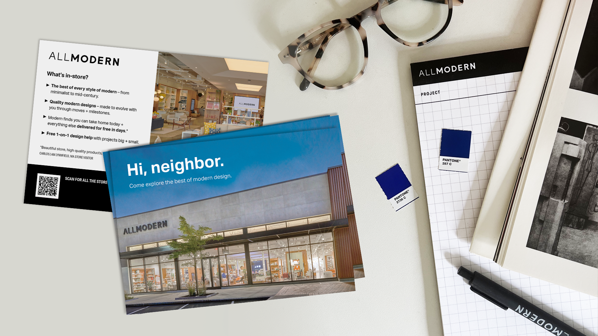 Two promotional cards for AllModern featuring modern design elements, alongside tortoiseshell glasses, a notepad, Pantone color swatches, and a pen on a light surface.