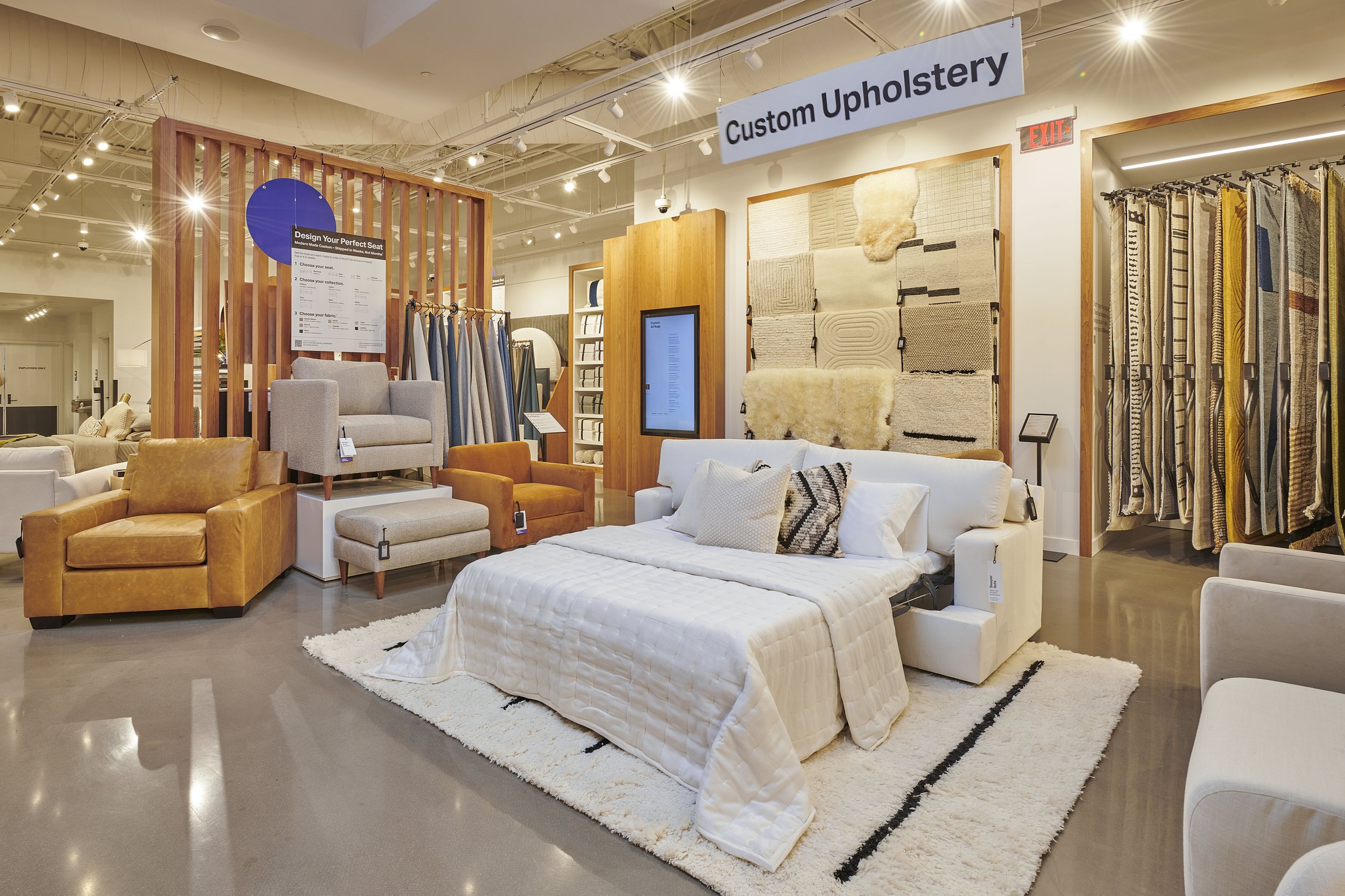Modern furniture store showcasing custom upholstery options, featuring a display of sofas, armchairs, and fabric samples. A sign reads "Custom Upholstery."