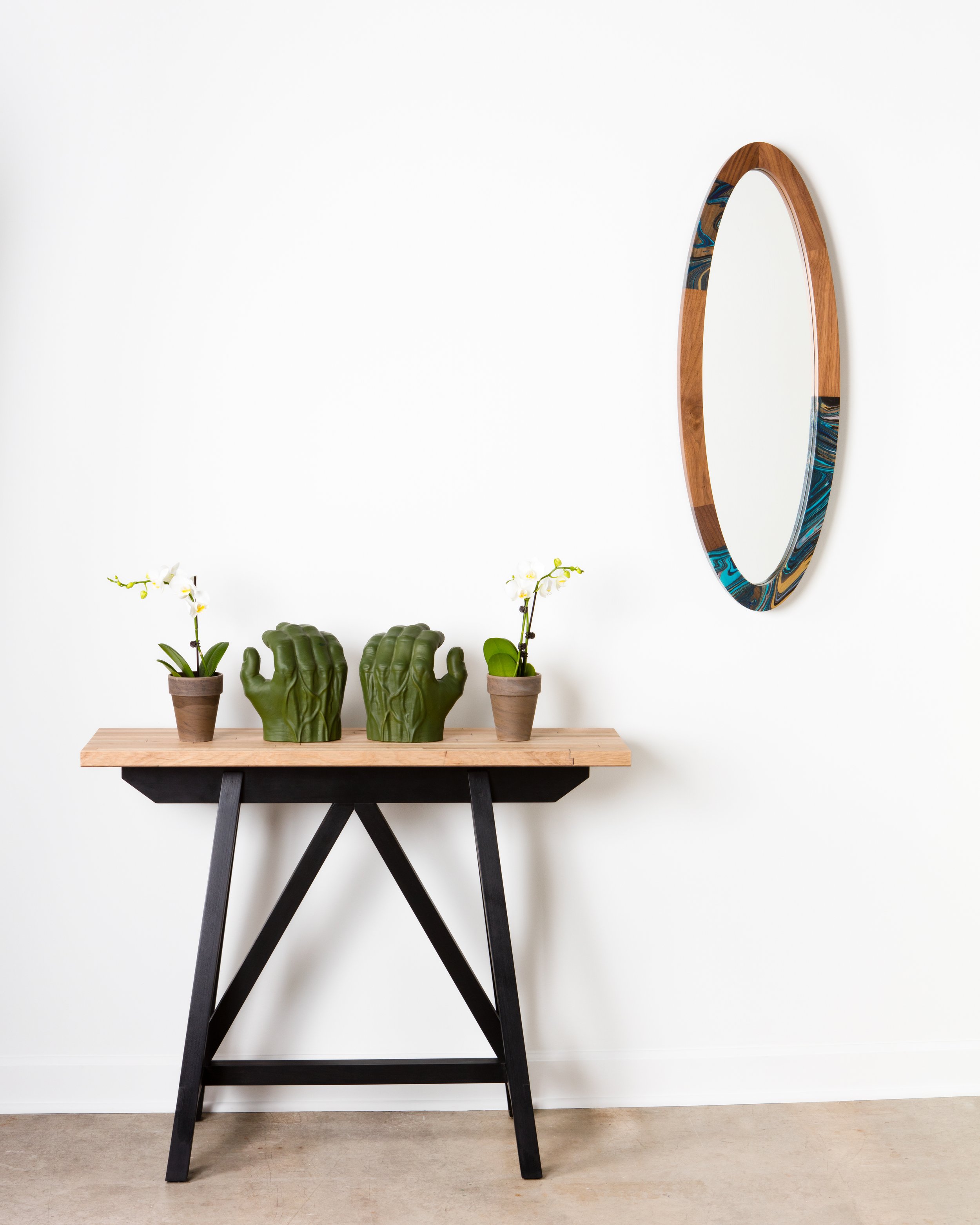 Context photo of the Finnley Marbleized Mirror mounted on the wall, next to a tall wooden bench with a hulk hand sculpture.