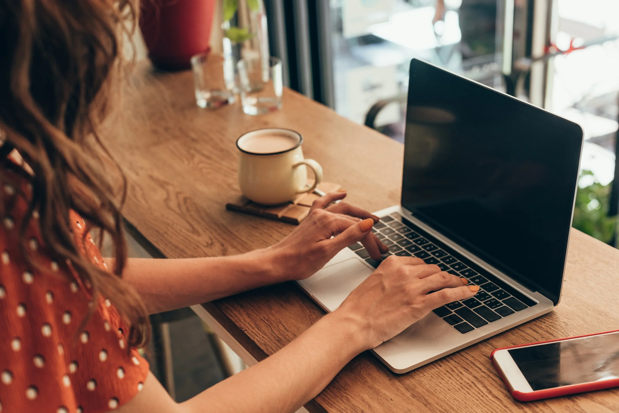 Hands working on a laptop next to a full cup of coffee