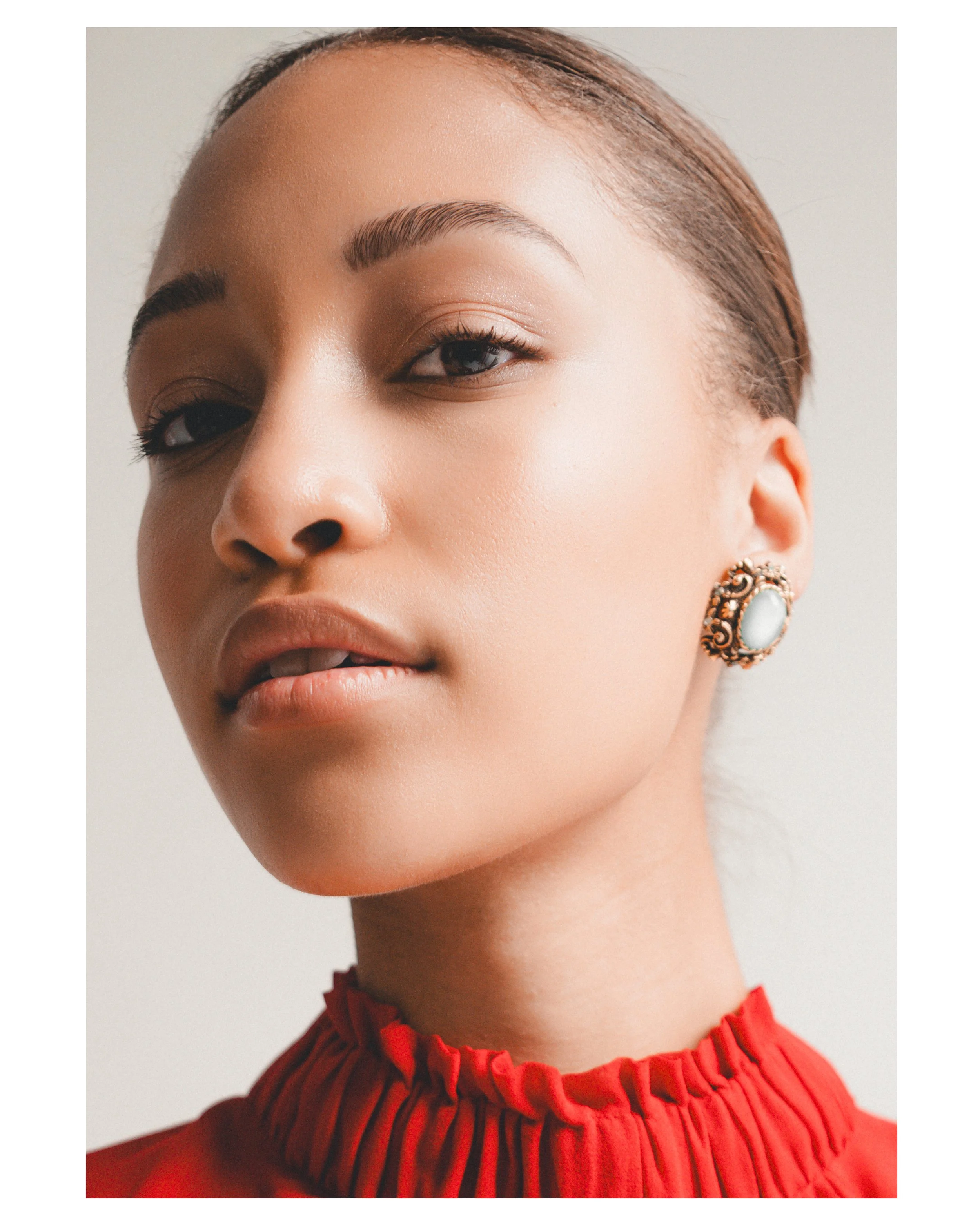 Close-up of a woman's face with makeup, wearing ornate earrings and a red pleated dress.