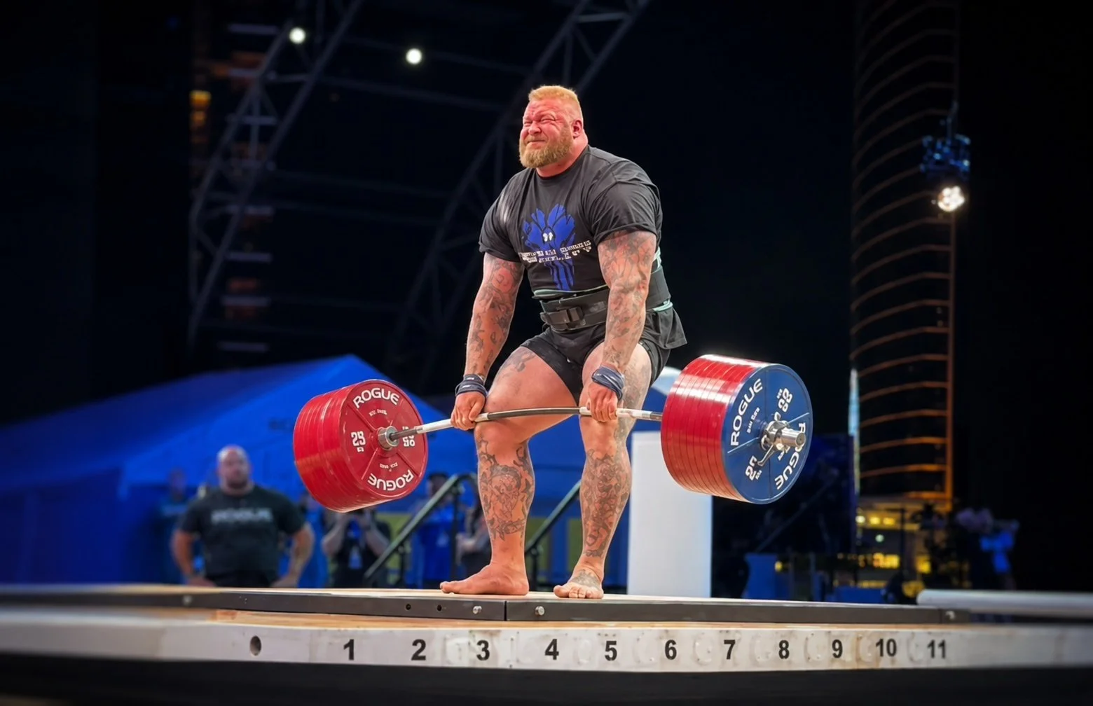 Hafþór Björnsson performs a heavyweight deadlift attempt on stage during an international strongman event with Rogue weight plates and dramatic night lighting.